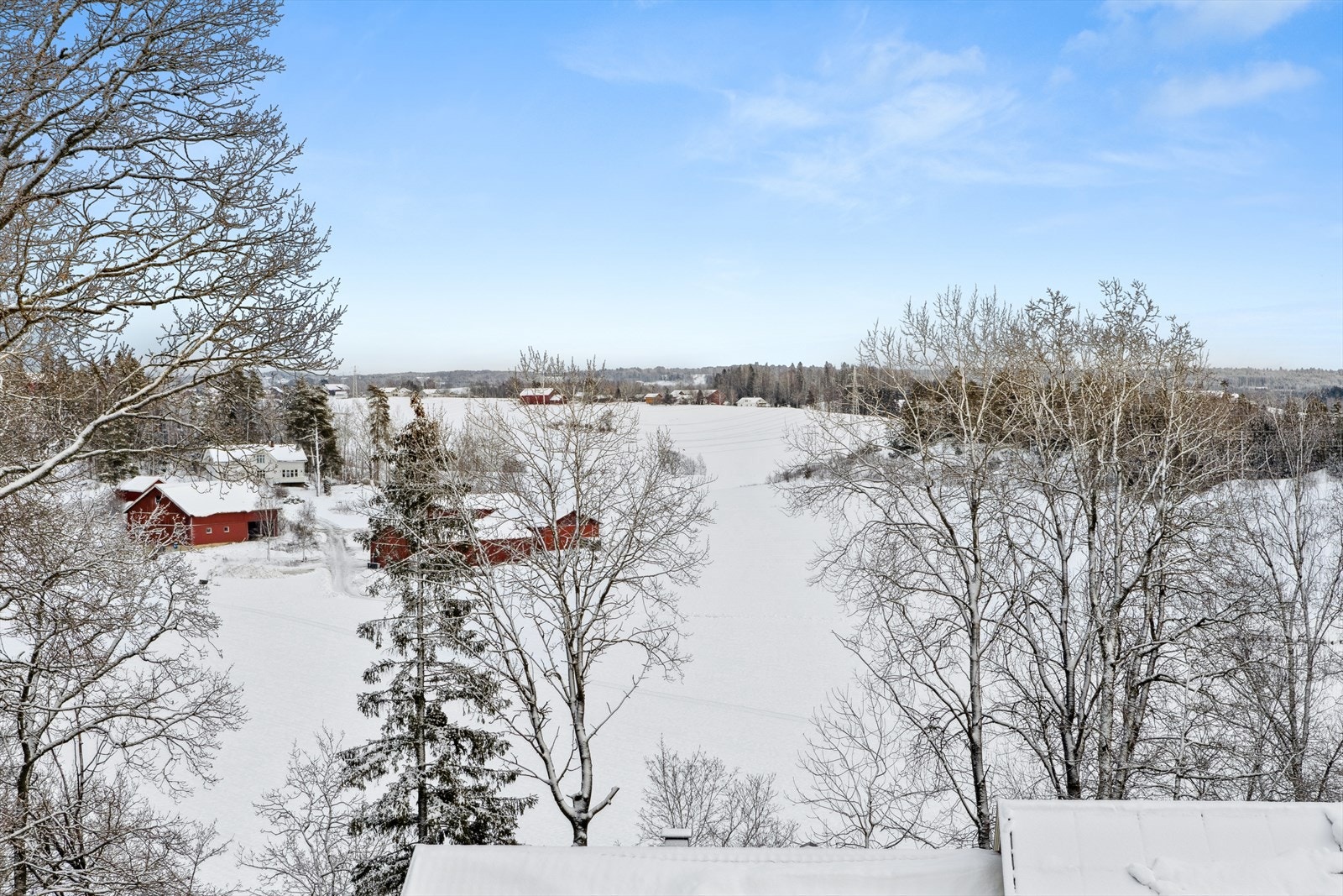 Vidstrakt utsikt mot åker hvor det er oppkjørte skiløyper om vinteren. Galleribilde