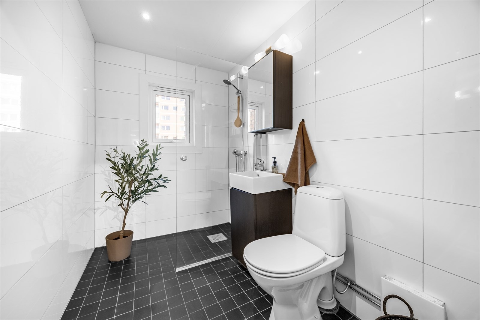 Flislagt bad med varmekabler i gulv. Baderomsinnredning bestående av benkeskap med glatte fronter og speilskap med belysning. Galleribilde