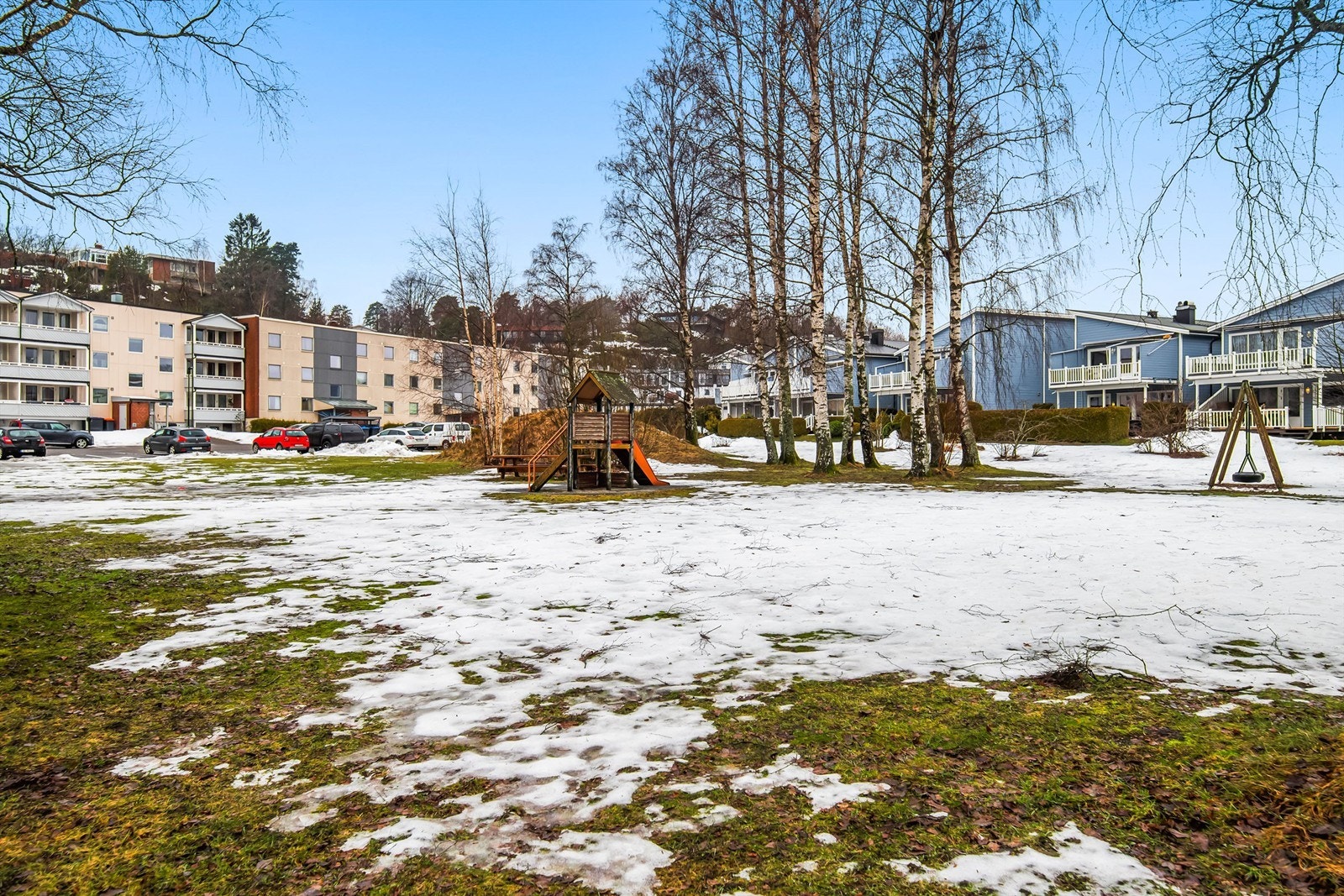 Stort åpent areal i fremkant av leiligheten med plen, naturlig vegetasjon og lekeplass Galleribilde