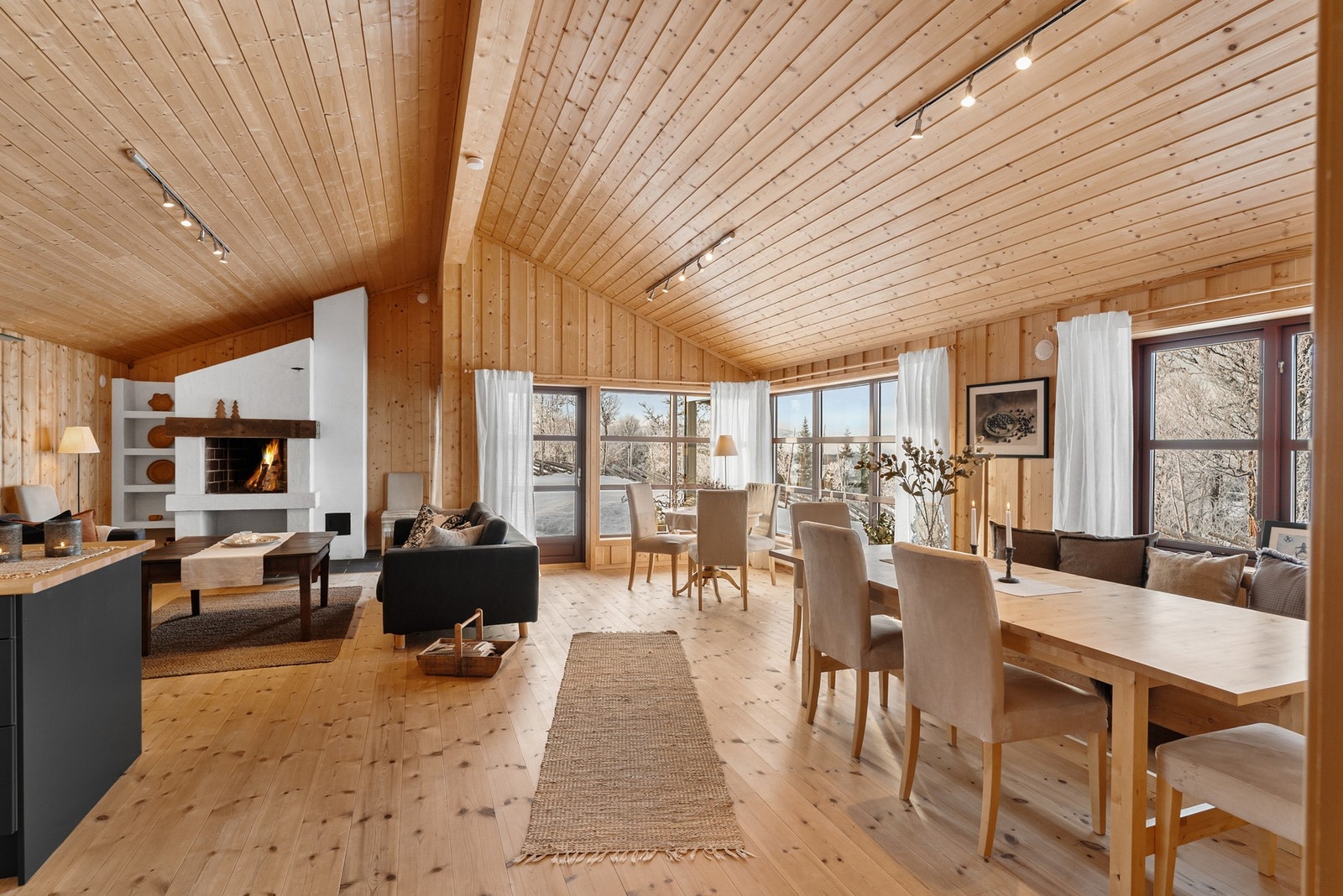 Videre kommer du inn i en romslig og innbydende stue. De store vinduene i kombinasjon med den gode takhøyden bidrar til at rommet oppleves som svært lyst og luftig. Galleribilde