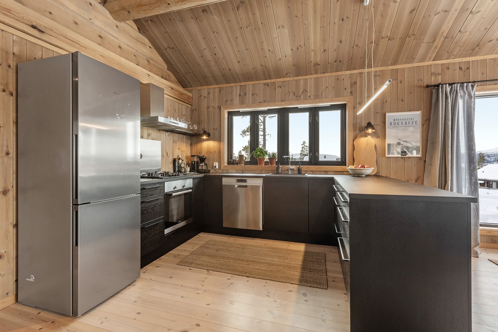 Kjøkkenet er innredet med sorte, glatte fronter, og en solid benkeplate av laminat. Her er det plass til et frittstående kjøl/fryseskap, oppvaskmaskin, komfyr og gassplatetopp. Galleribilde