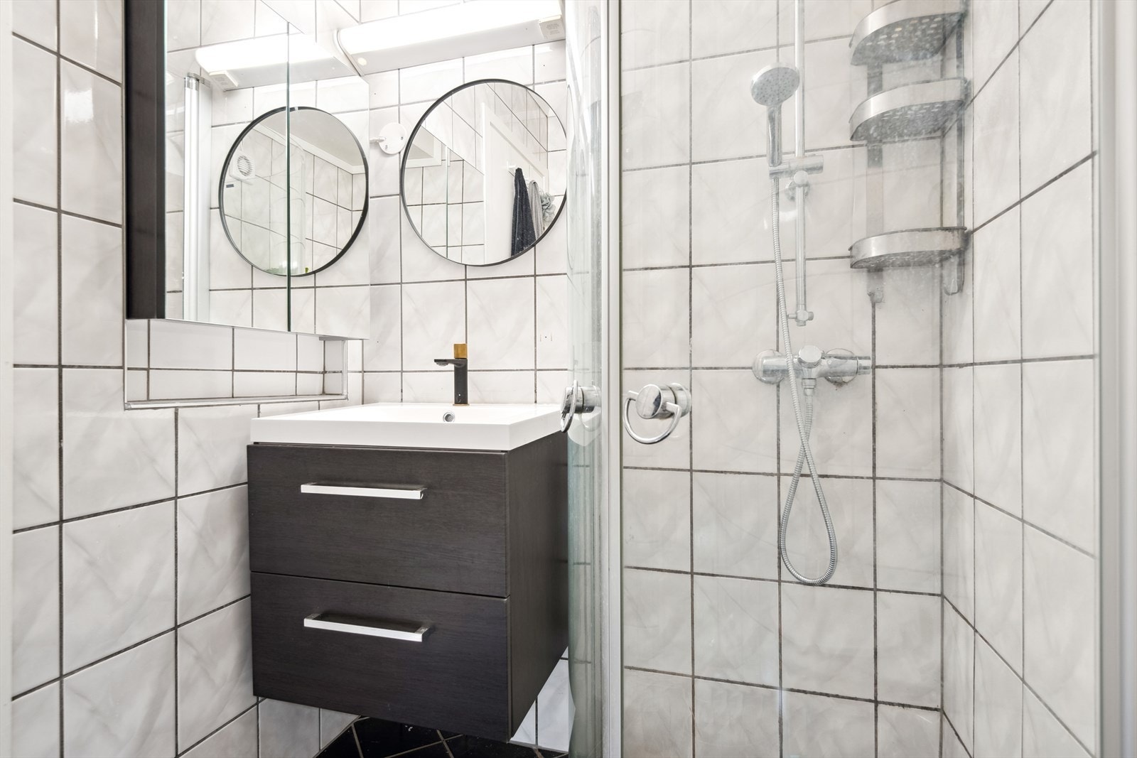 Badet er av klassisk utførelse, og inneholder toalett, dusjhjørne og servant med skapinnredning Galleribilde