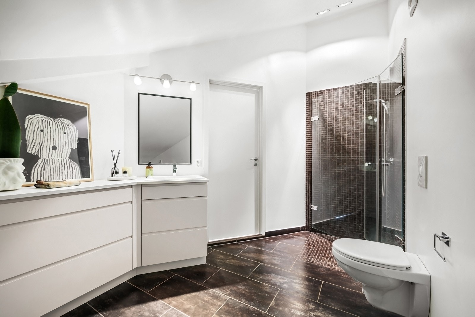 Badet er fra 2009 med en kombinasjon av flislagte og slette flater. Innredningen i rommet består av dusj med svingbare glassvegger, vegghengt toalett og servant med skuffer. Galleribilde