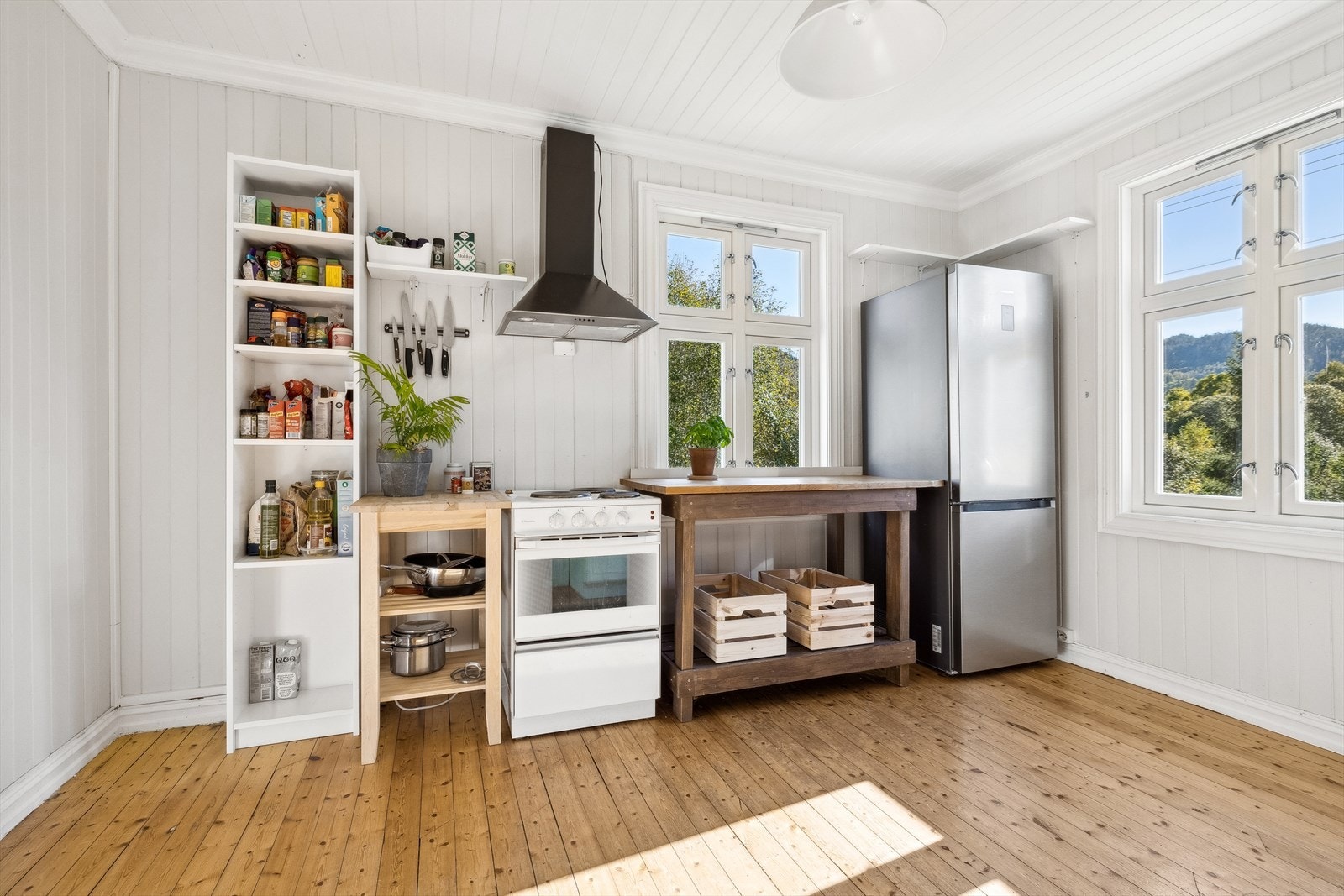 Koselig og luftig kjøkken med frittstående kjøkkenbenk, komfyr og kjøleskap. Galleribilde