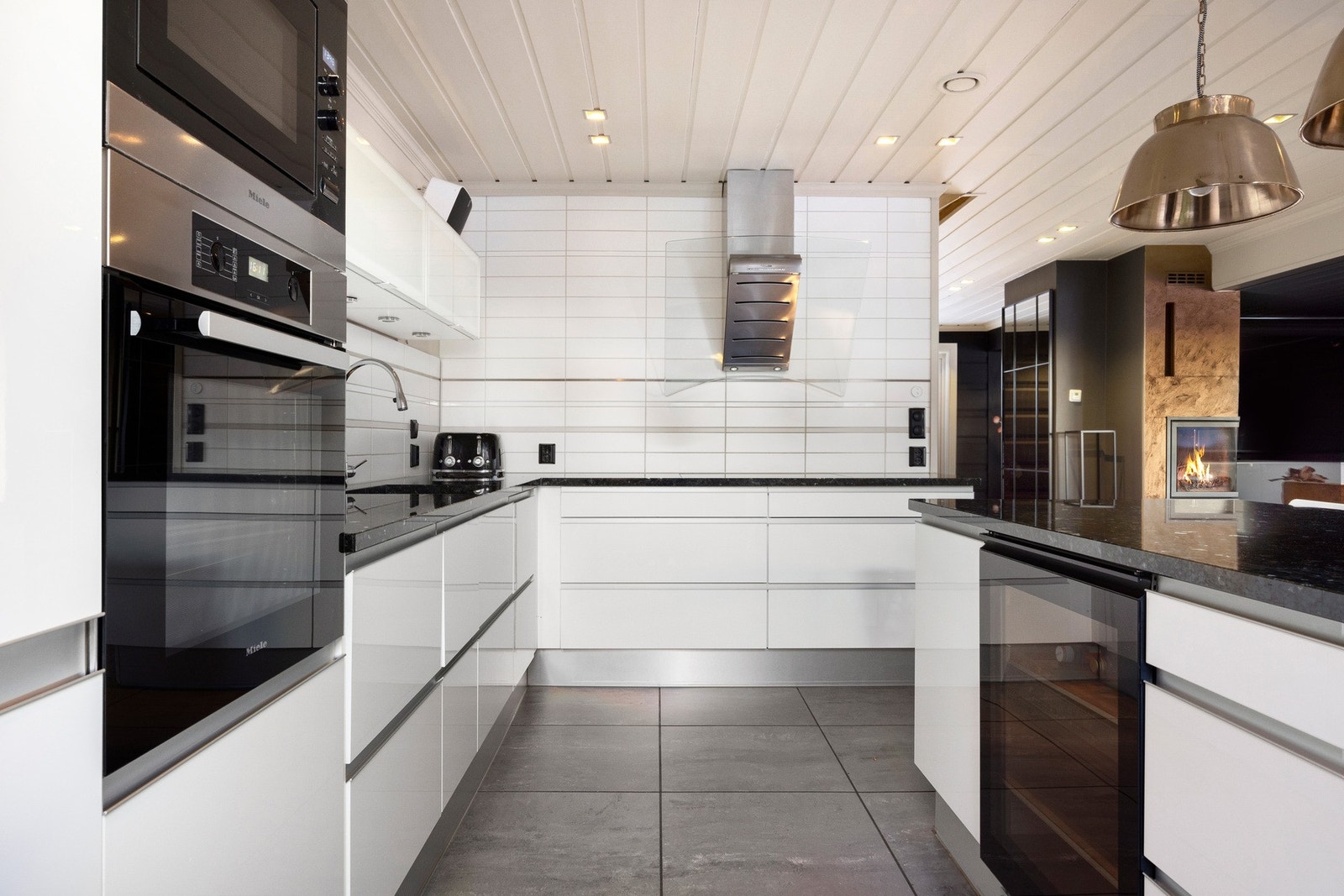 Benken har en underlimt oppvaskkum i stål og planlimt induksjonstopp. Stekeovn og mikrobølgeovn fra Miele som er praktisk montert i et høyskap. Galleribilde