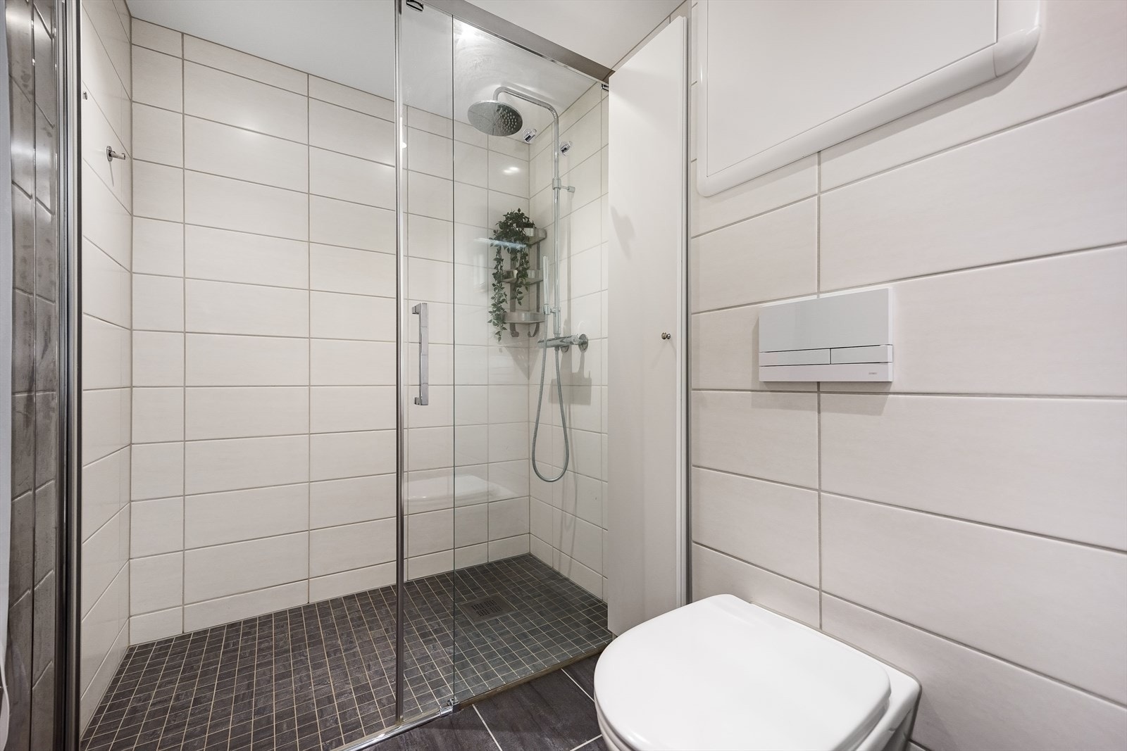 Badet er innredet med servant med speil og belysning, vegghengt toalett og dusjsone med skyvedør i glass Galleribilde