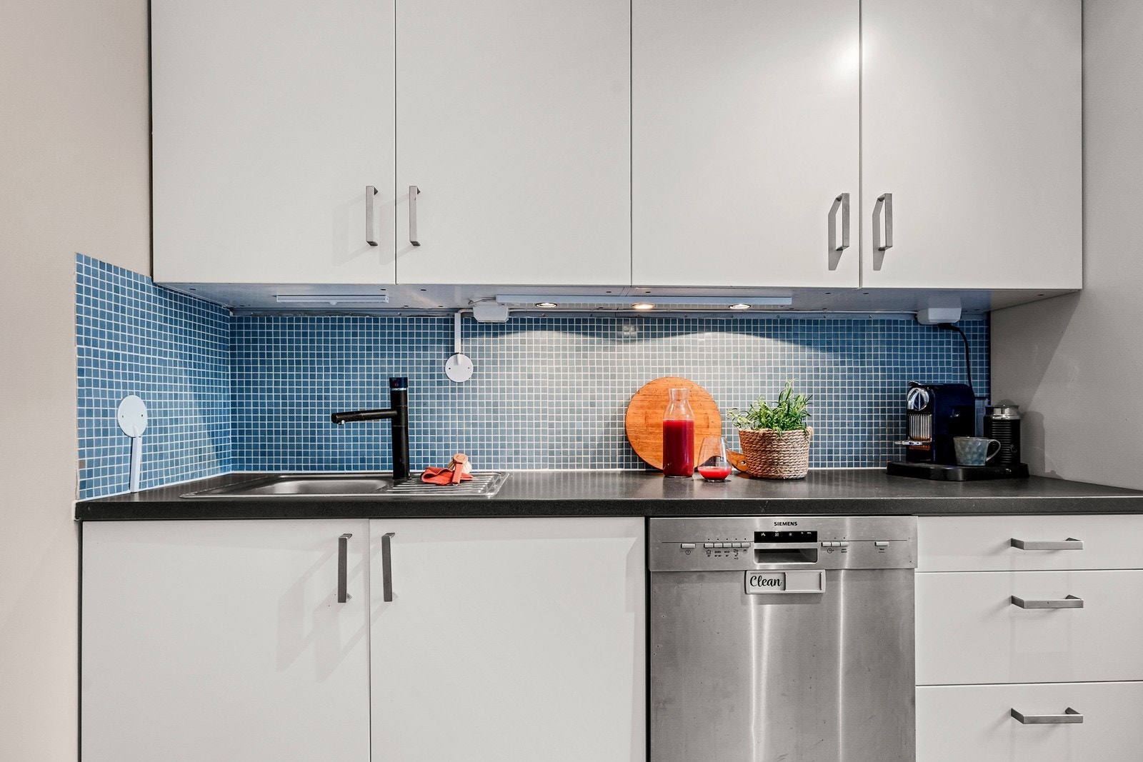 Benkeplaten i laminat har nedfelt servantkum, over benk er det mosaikkflis og under overskap er det montert lyslist. Galleribilde