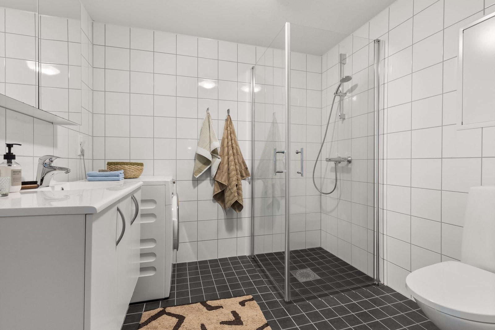 Badet er pent flislagt på gulv og vegger med varme i gulvet. Badet har dusjhjørne med svingbare glassdører. Det er opplegg for vaskemaskin. Galleribilde