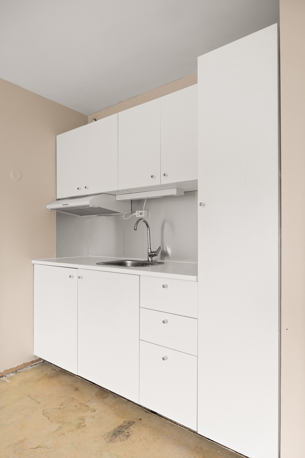 Hybelkjøkken med slette fronter og nedfelt vask. Det er ikke avsatt plass til hvitevarer, men over den naturlige plassen for komfyr er det montert ventilator med kullfilter Galleribilde