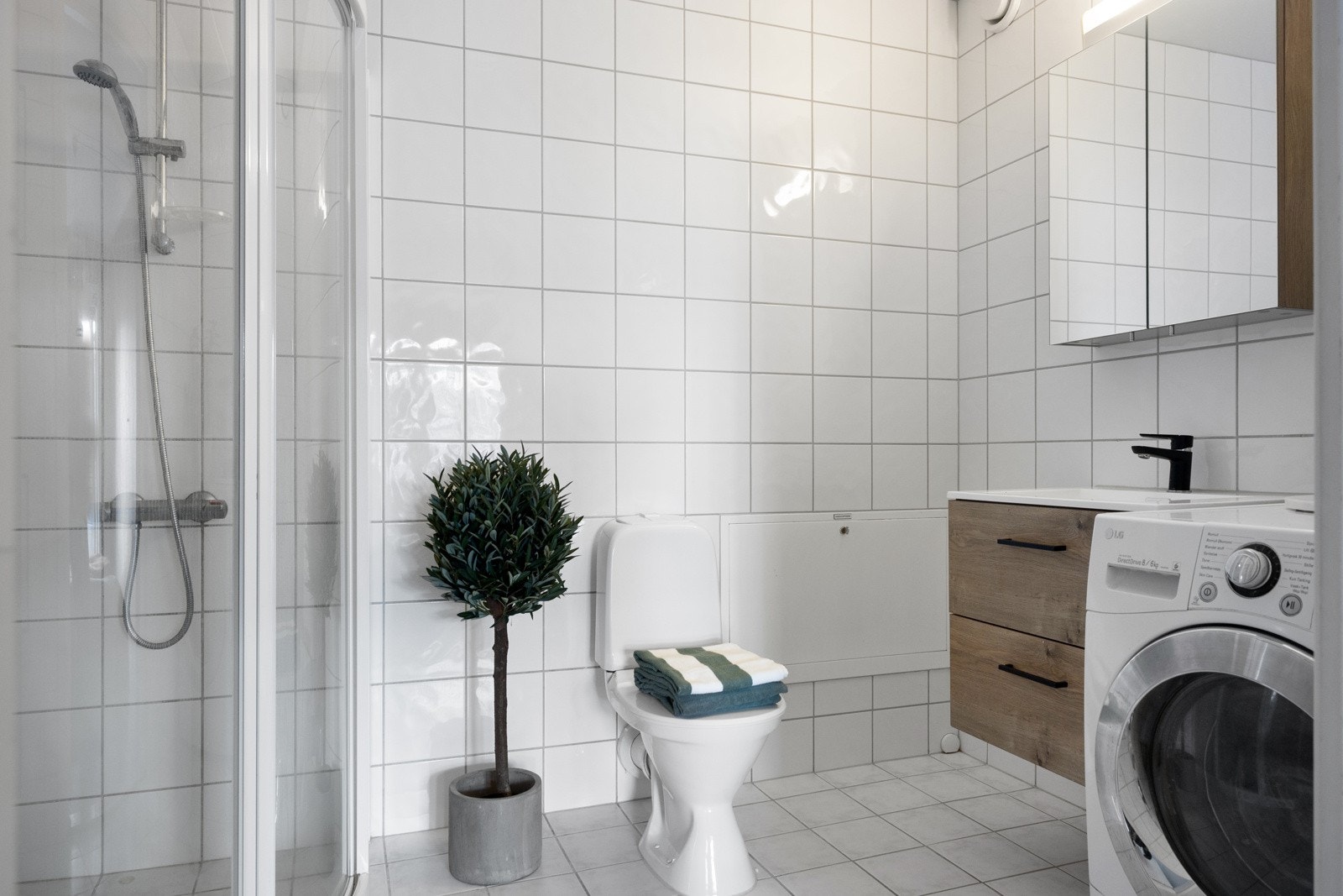 Stilrent bad med fliser på gulv og vegger samt behagelig gulvvarme. Praktisk dusjhjørne med skyvedører og termostatstyrt dusjbatteri i krom med hånddusj. Veggmontert servantinnredning med heldekkende vask Galleribilde