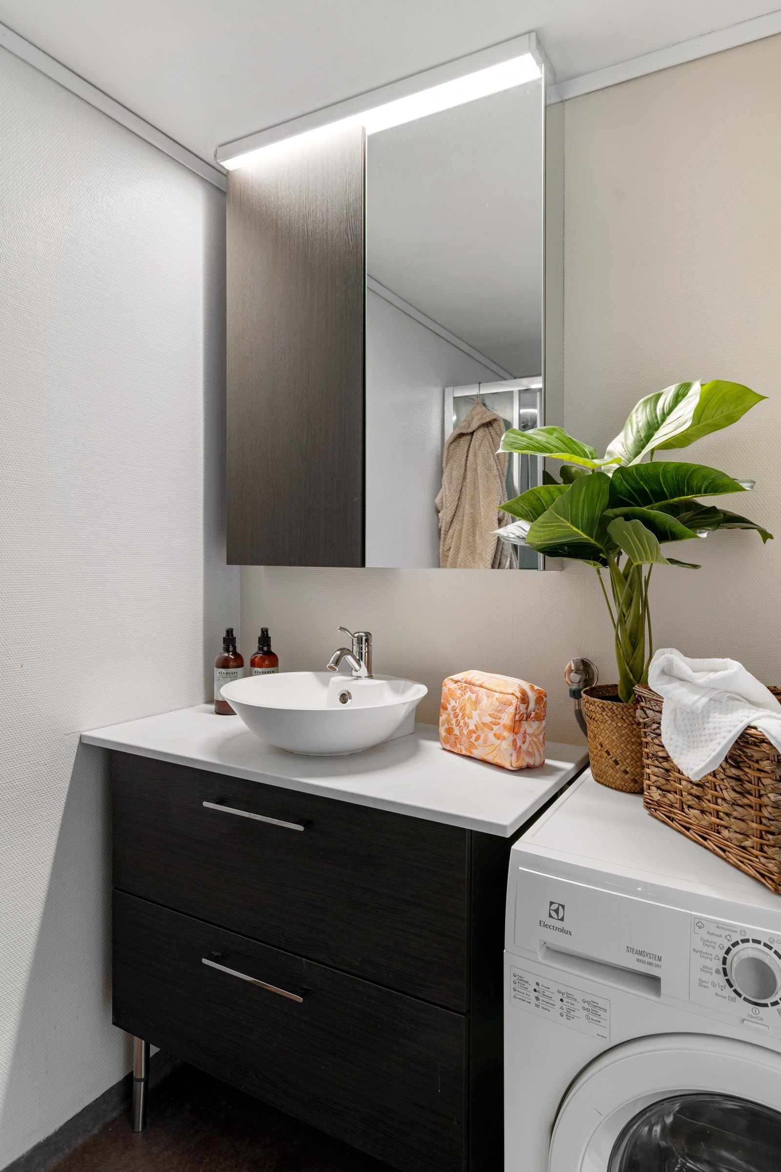 Badet har en nyere servant, med en mørk innredning med speilskap, belysning samt opplegg for vaskemaskin Galleribilde