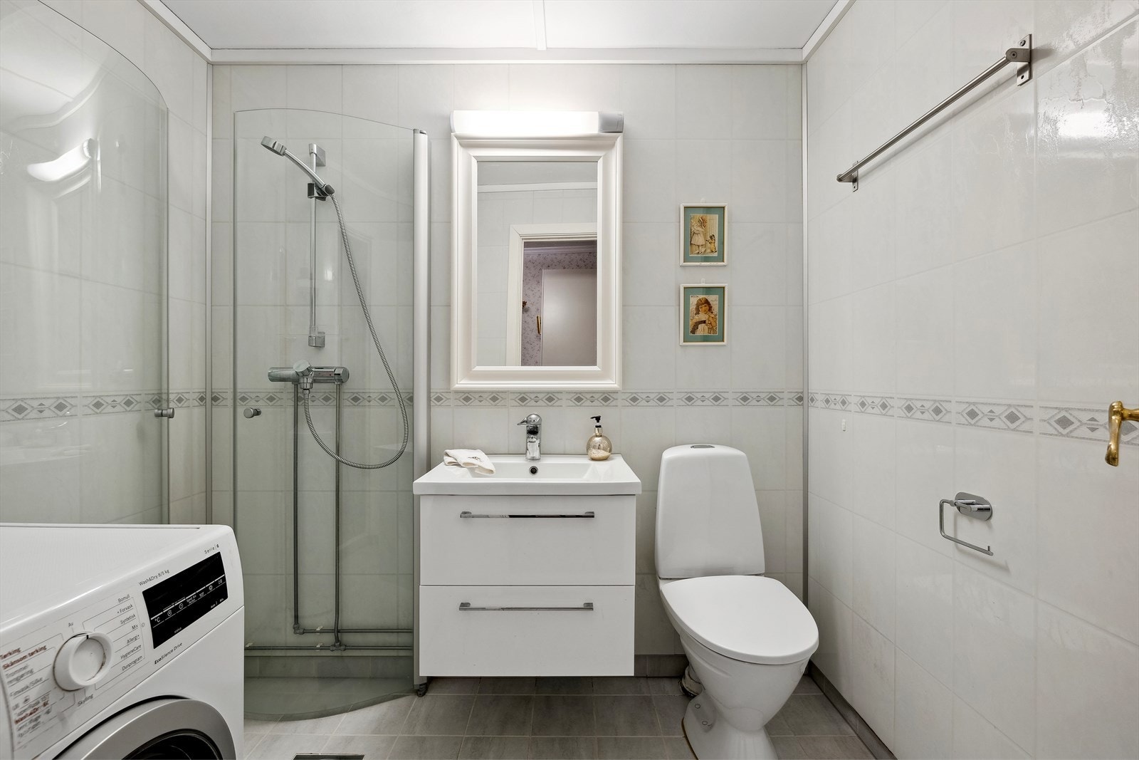 Lyst og moderne flislagt bad med dusj og vaskemaskin. Praktisk innredning og stilrene detaljer Galleribilde