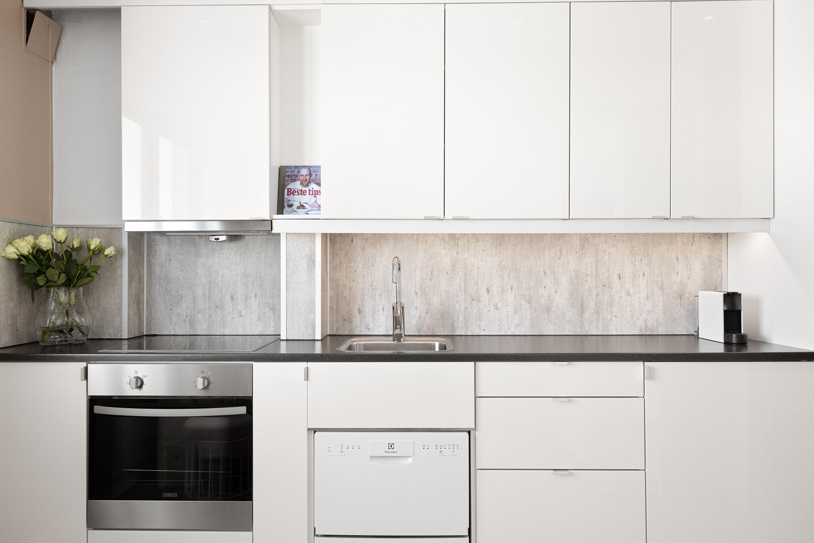 Her har du en tidsriktig kjøkkeninnredning med hvitevarer som komfyr, oppvaskmaskin, induksjonstopp, og kjøleskap. Galleribilde