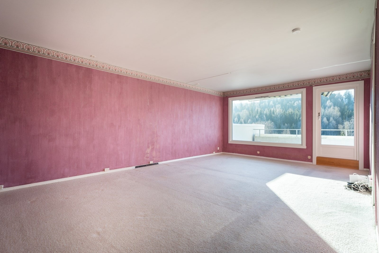 Leiligheten har en romslig stue som også har en noe utdatert stil, med teppe på gulvet og mørkmalte vegger. Det er likevel ingen tvil om at rommet har potensial, og det er god plass til både sofagruppe og spisebord. Galleribilde