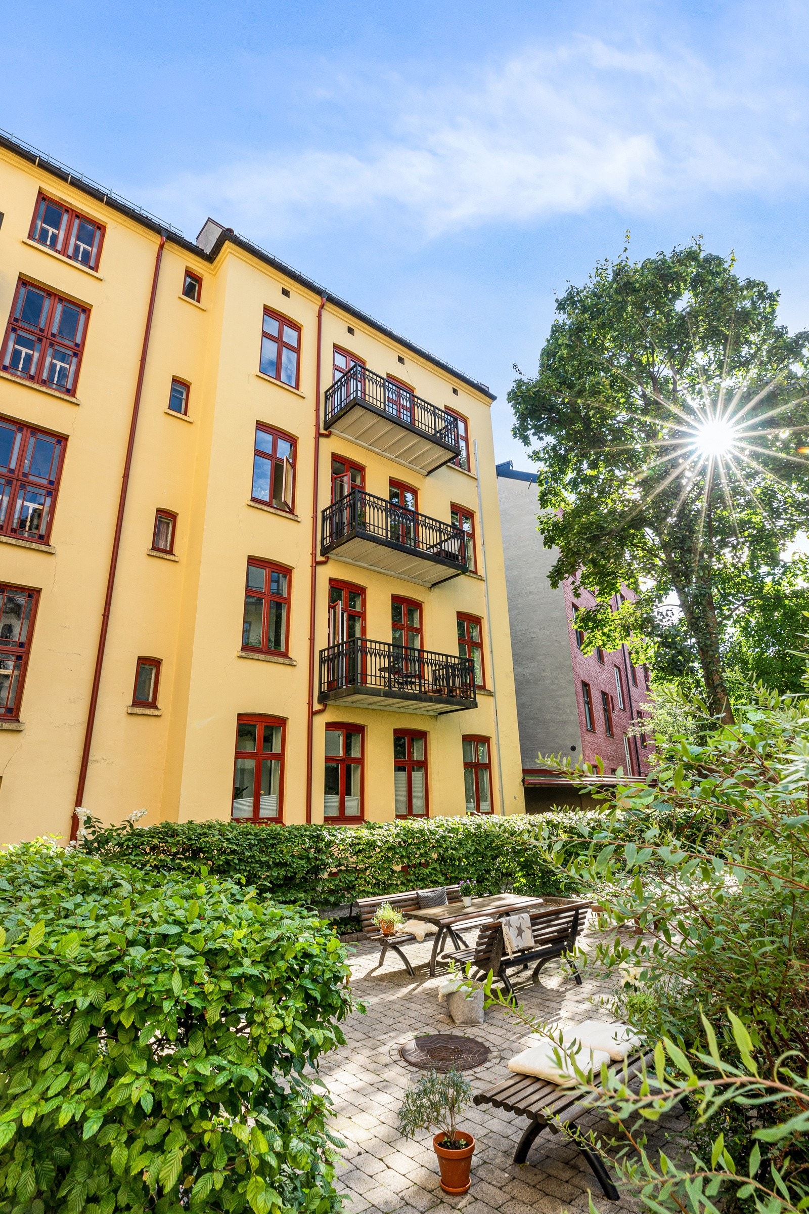 Bakgården består av brosteinsbelagt grunn, grus, gressplen, flere sittegrupper, søppelskur, sykkelparkering samt diverse busker og beplantinger Galleribilde