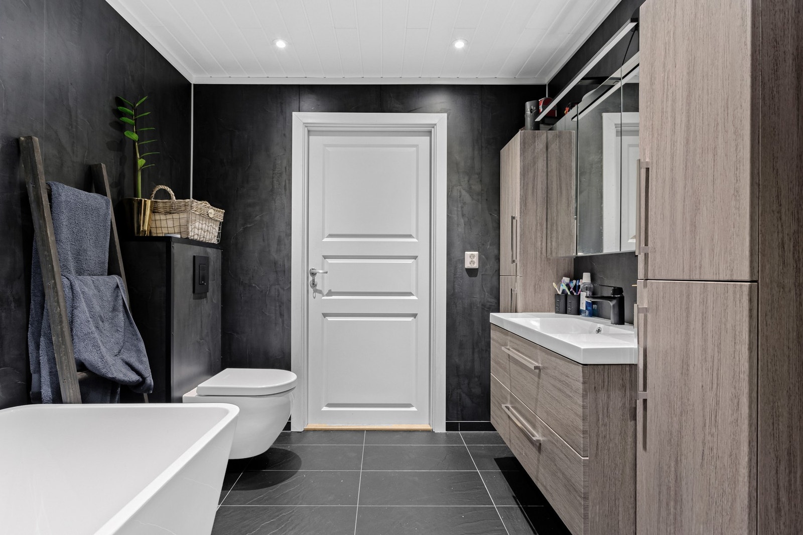 Badet har vegghengt toalett, dusjnisje, badekar og en elegant servant. Mørke vegger kombineres med lyst interiør for et lekkert uttrykk. Galleribilde