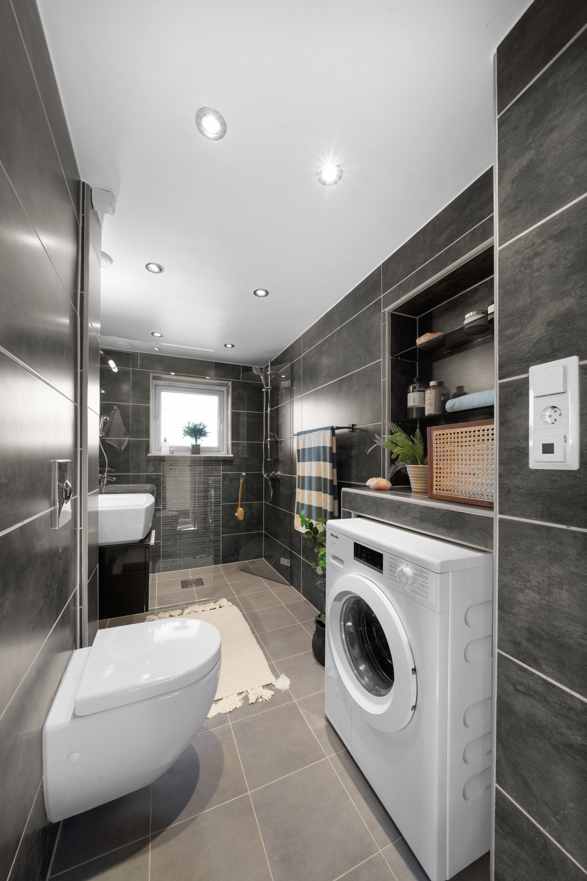 Badet fremstår som et moderne og elegant rom med mørke fliser som gir et eksklusivt uttrykk. Galleribilde