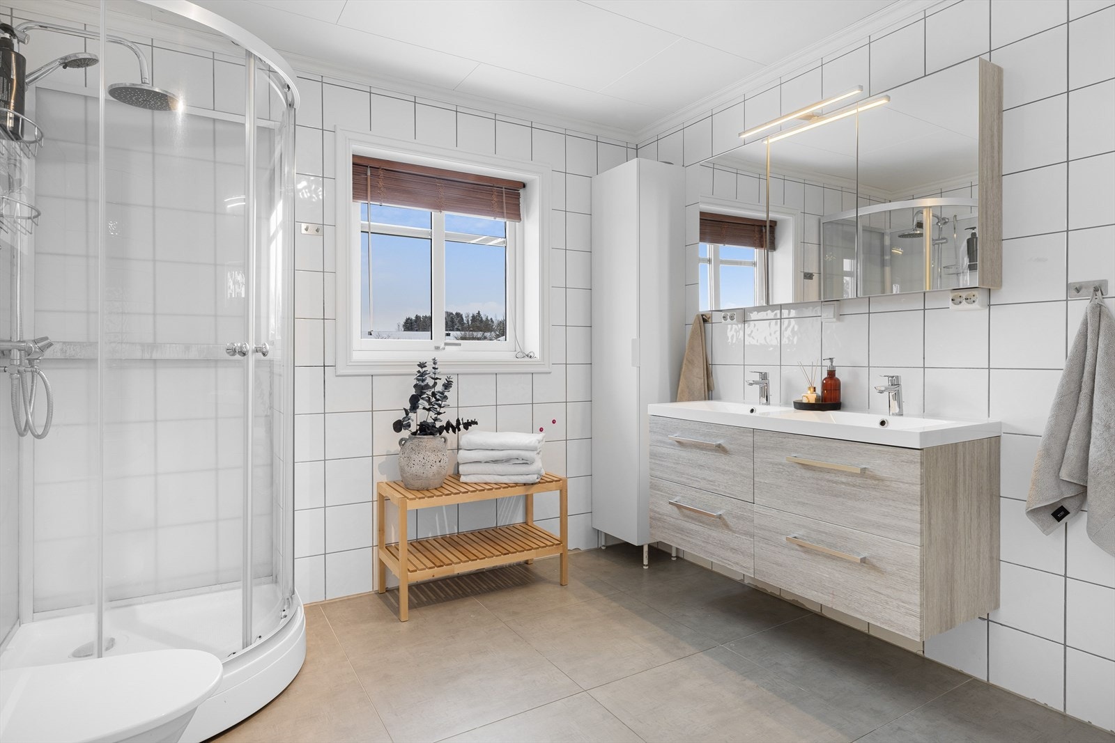 Moderne baderomsinnredning med skuffer og heldekkende dobbel servant, stort speilskap med belysning over, samt ekstra høyskap ved siden av. Galleribilde