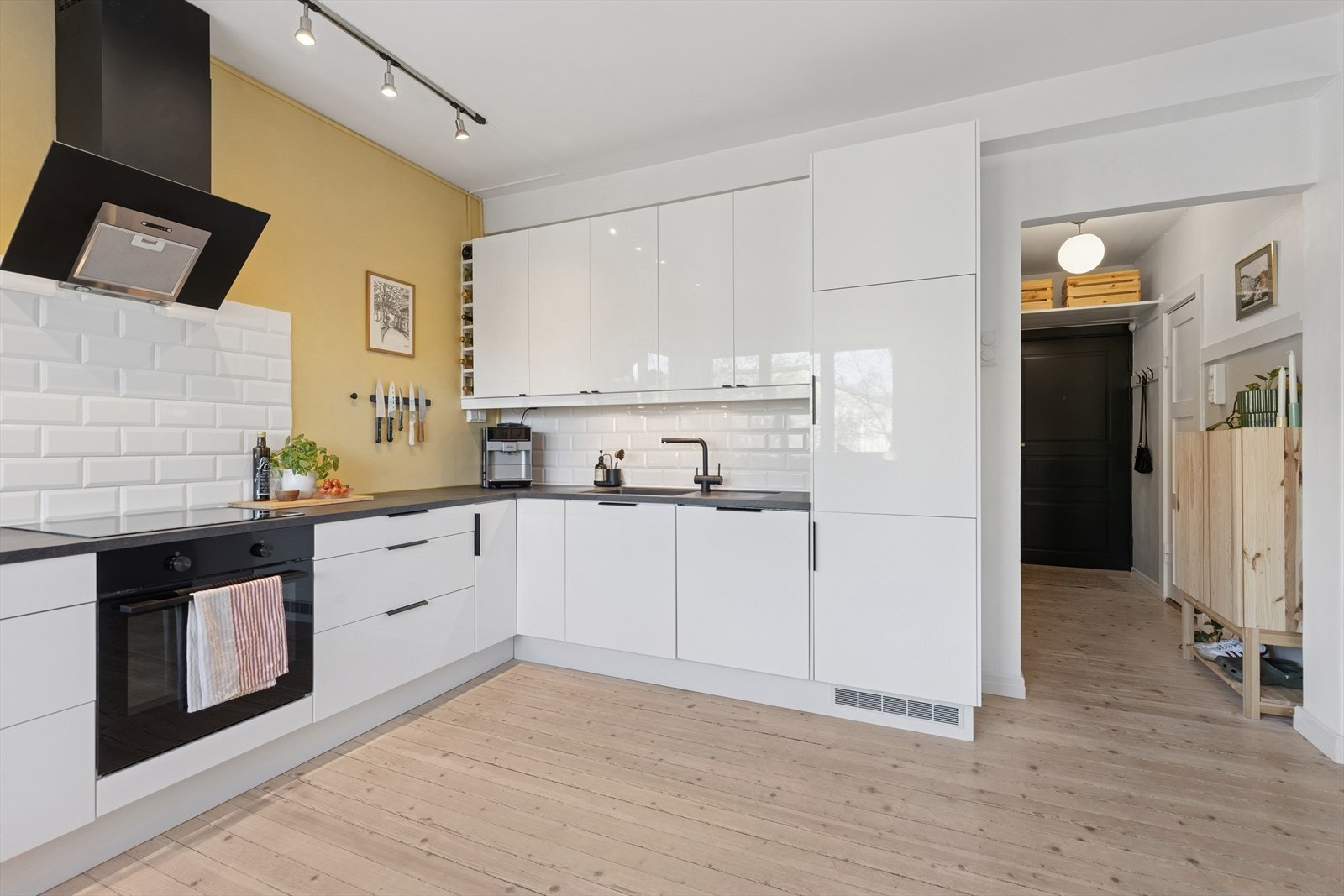 Kjøkkenet er innredet med glatte, høyglans fronter, laminat benkeplate med planlimt kum i kompositt og fliser på vegg over benk. Galleribilde