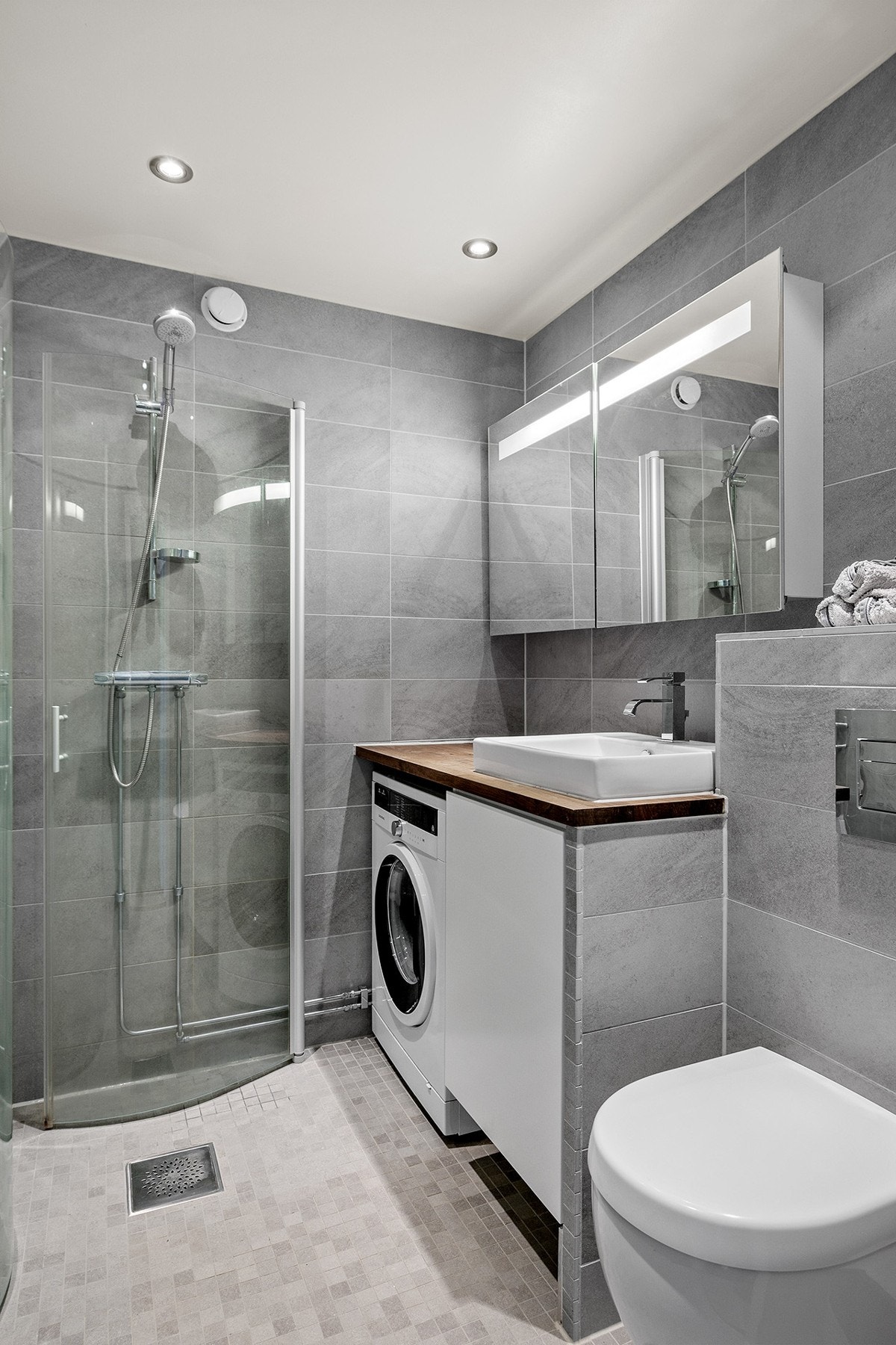 Baderomsinnredningen er bestående av heltre benkeplate med toppmontert servant, speilskap med overlys, vegghengt klosett, dusjhjørne med svingbare glassdører og opplegg for vaskemaskin. Galleribilde