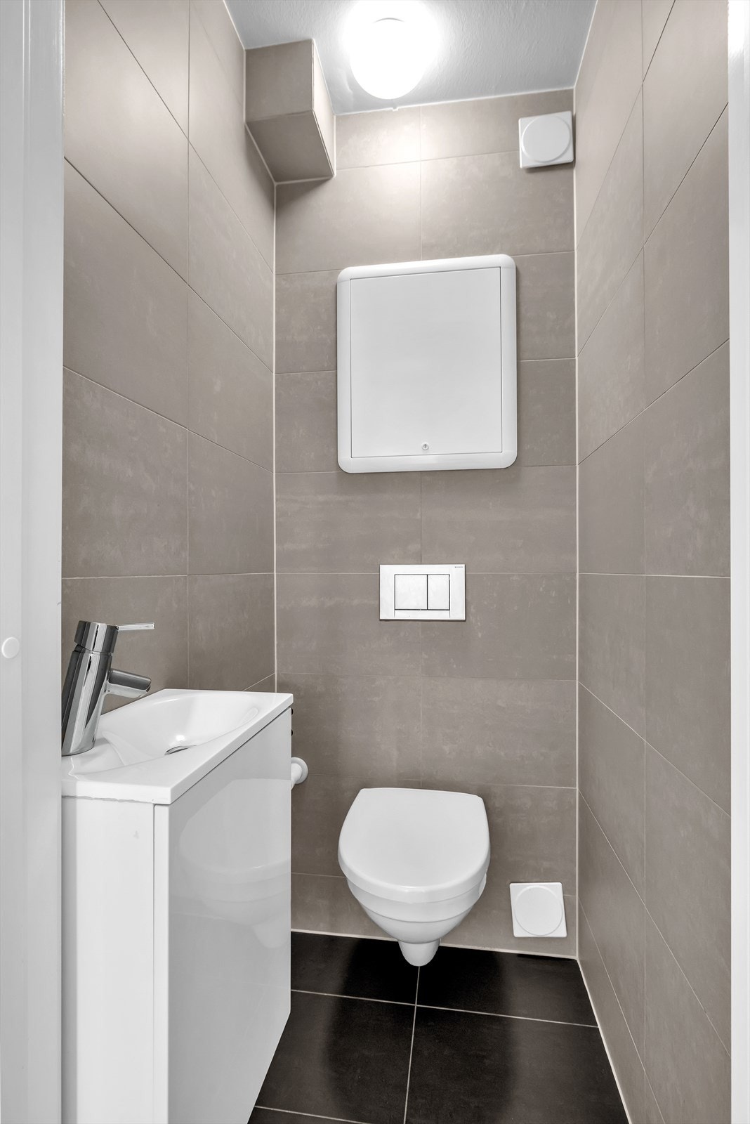 WC rett ved siden av badet, også flislagt, vegghengt toalett med innebygd sisterne samt servant Galleribilde