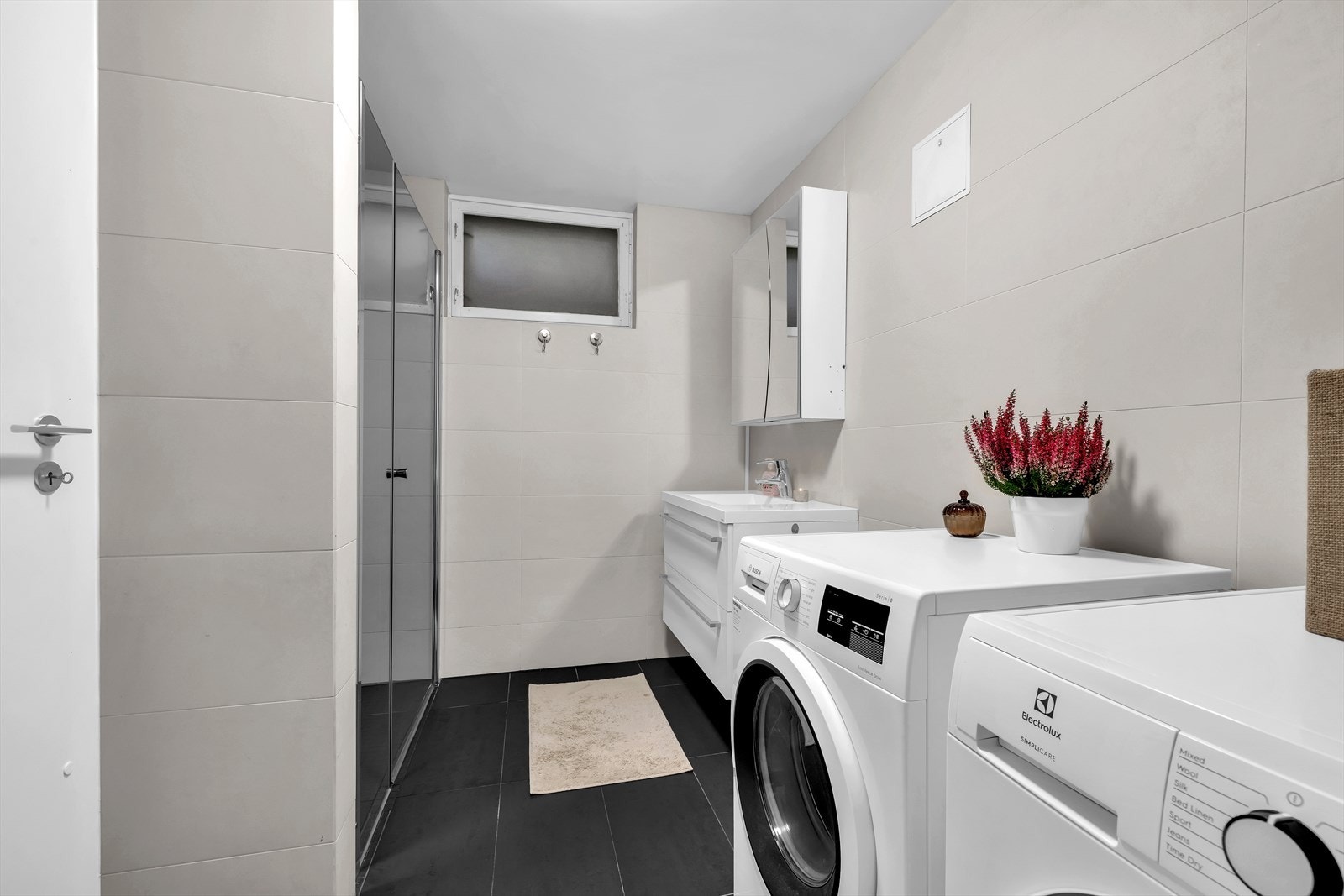 Badet har veggfestet toalett, servant med speilbelagt veggskap samt dusjhjørne Galleribilde