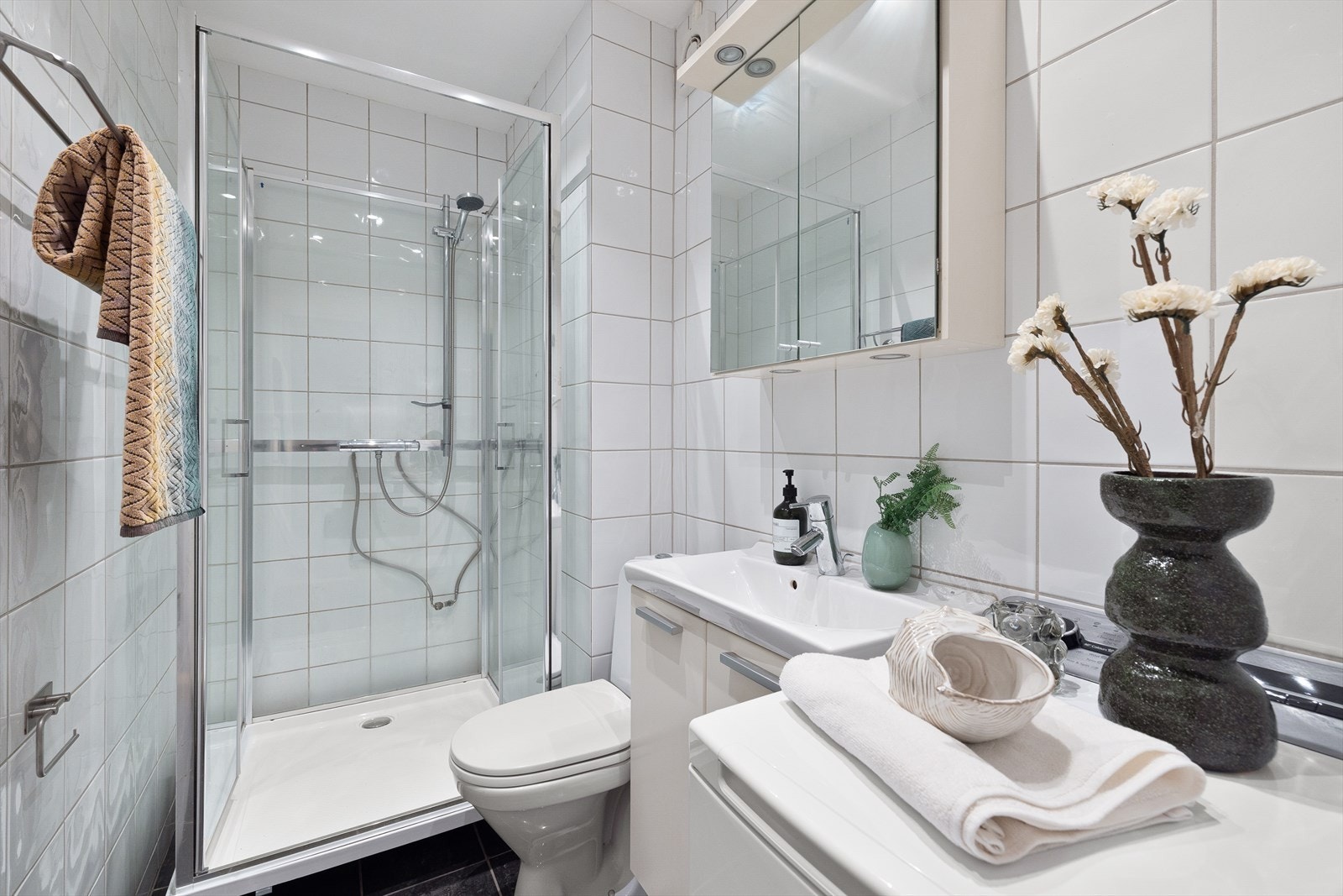 Badet er utstyrt med gulvstående toalett, dusjkabinett samt baderomsinnredning med skap, keramisk servant med ettgreps blandebatteri fra Hans Grohe og overskap. Galleribilde