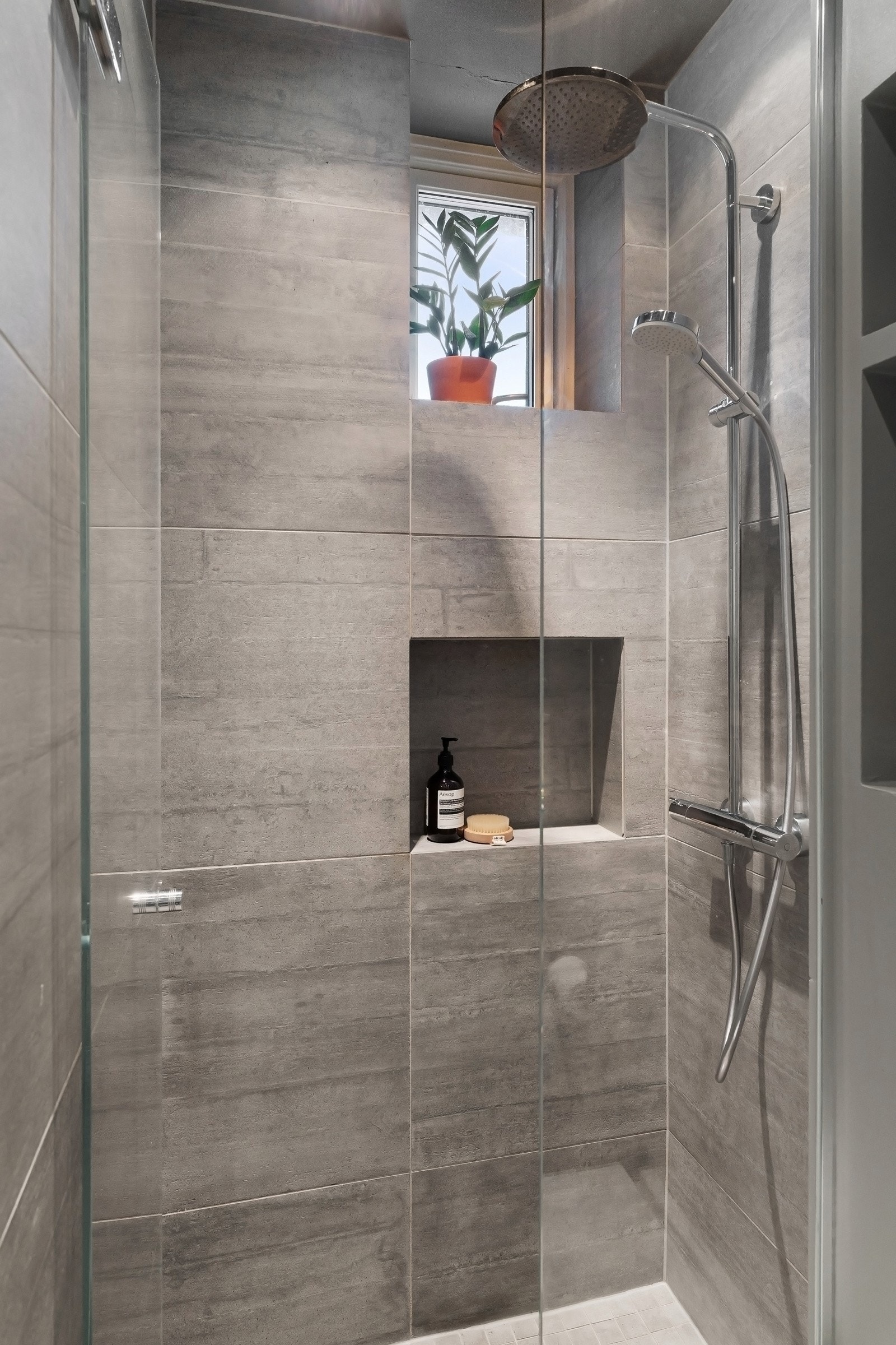 Dusjsone adskilt med glassvegg og dør, stilren dusjgarnityr med regnfallsdusj og hånddusj. Praktisk nisje for dusjartikler. Galleribilde