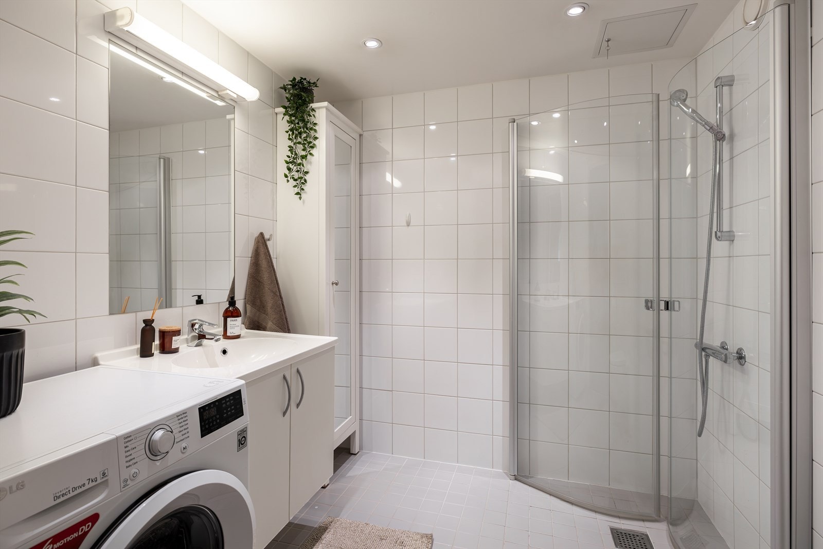 Delikat og flislagt baderom med dusjnisje med innfellbare dusjdører, servant med ett greps blandebatteri og vegghengt toalett. Galleribilde