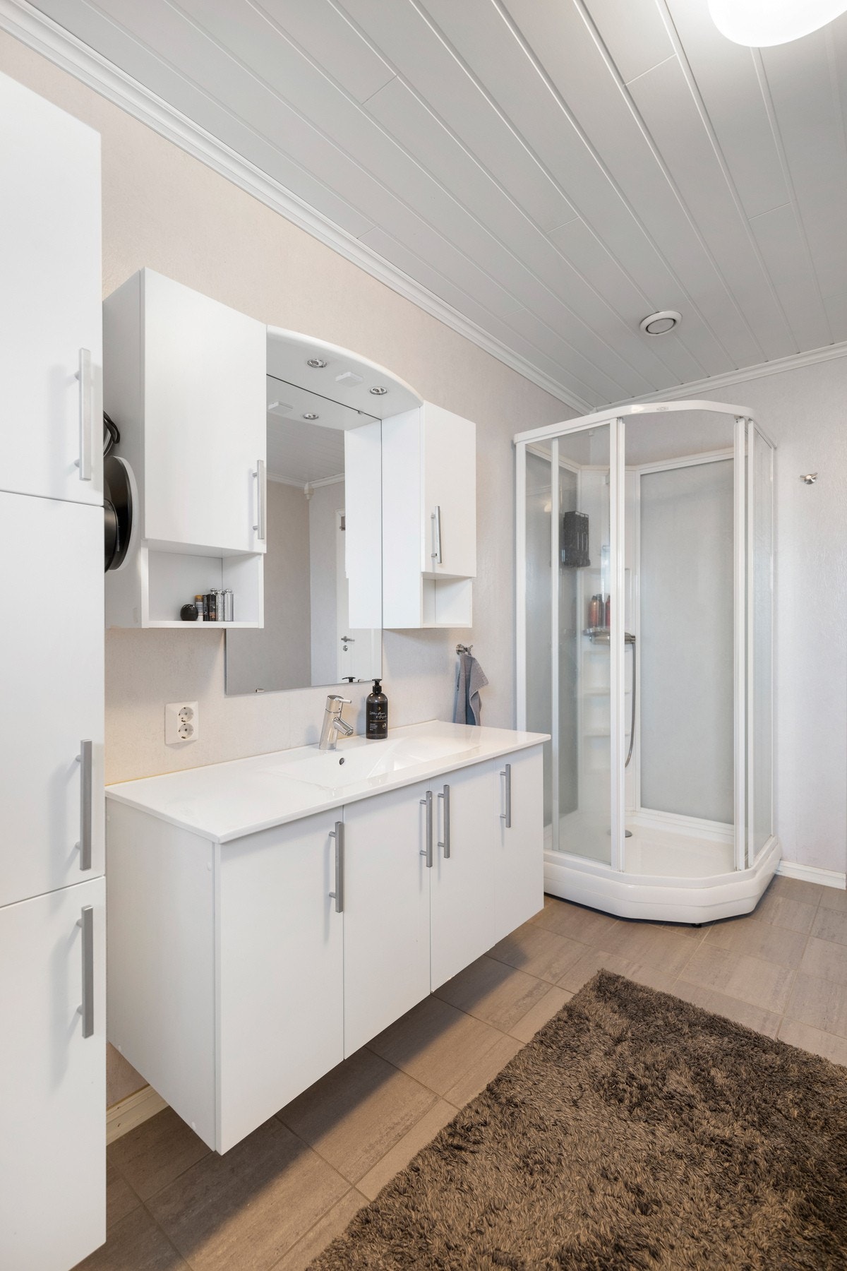 Rommet er utstyrt med dusjkabinett, vegghengt toalett og baderomsinnredning med servant og speil. Galleribilde