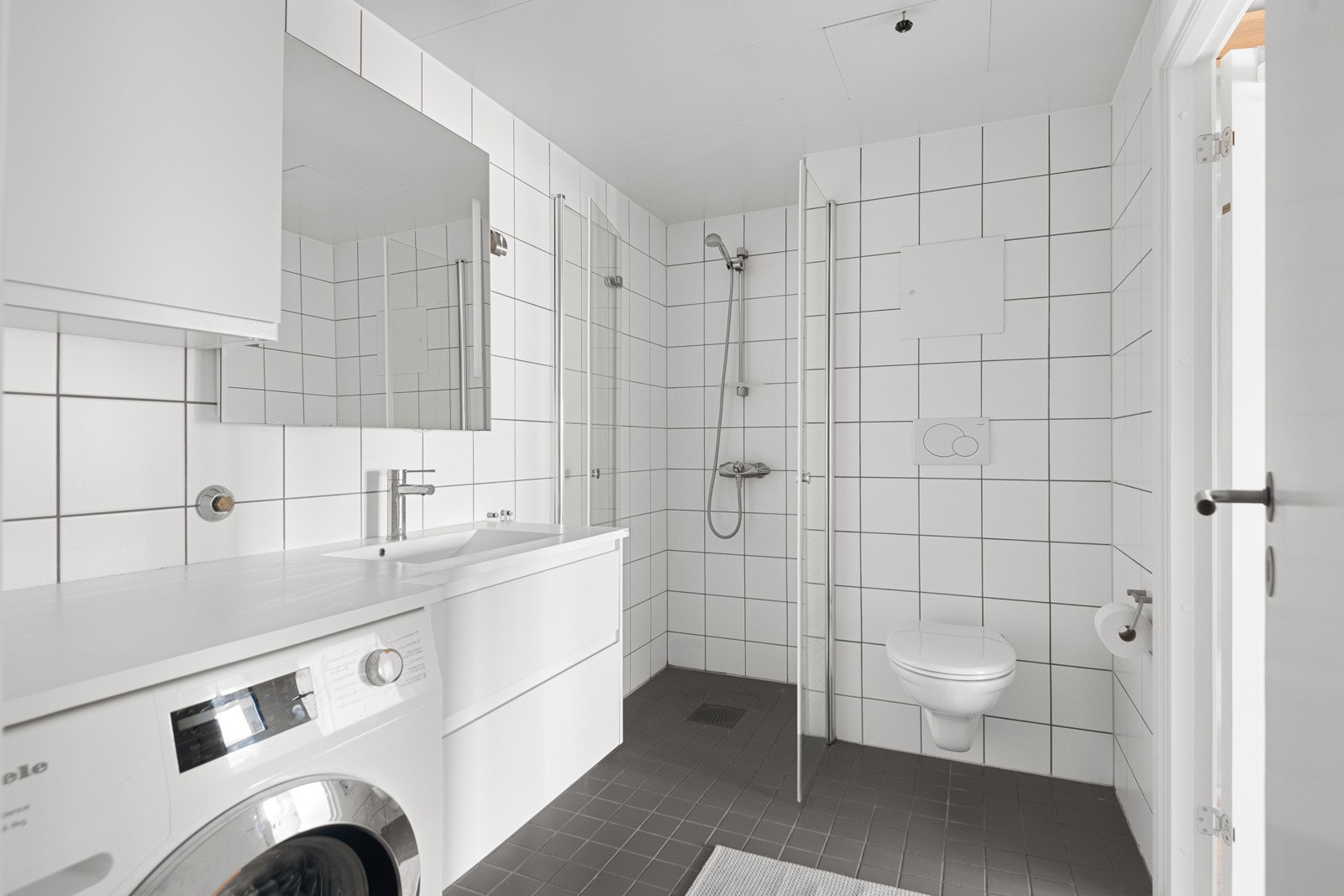 Leiligheten har et lyst og moderne baderom fra byggeåret 2005 som har adkomst både fra hovedsoverommet og entréen. Baderommet har grå fliser på gulv med gulvvarme, hvite fliser på veggene og mekanisk avtrekk. Galleribilde