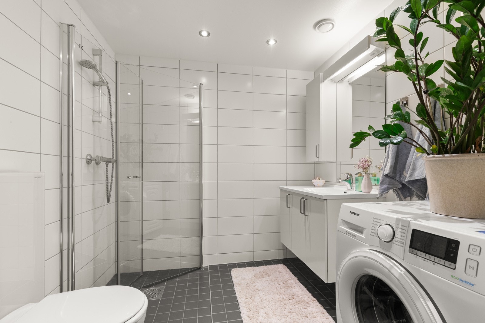 Pent flislagt baderom med behagelig varme i gulv og downlights i himling. Badet er utstyrt med vegghengt wc, dusjnisje med innfellbare glassdører, vegghengt servantskap med helsøpt servant og overskap med speil. Galleribilde
