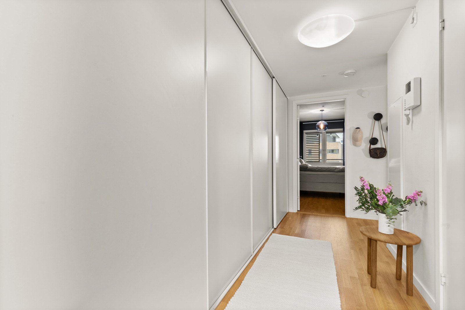 En romslig entré med plassbygd hvit skyvedørsgarderobe langs den ene langveggen som sørger for rikelig med oppbevaringsplass for sko og yttertøy. Galleribilde