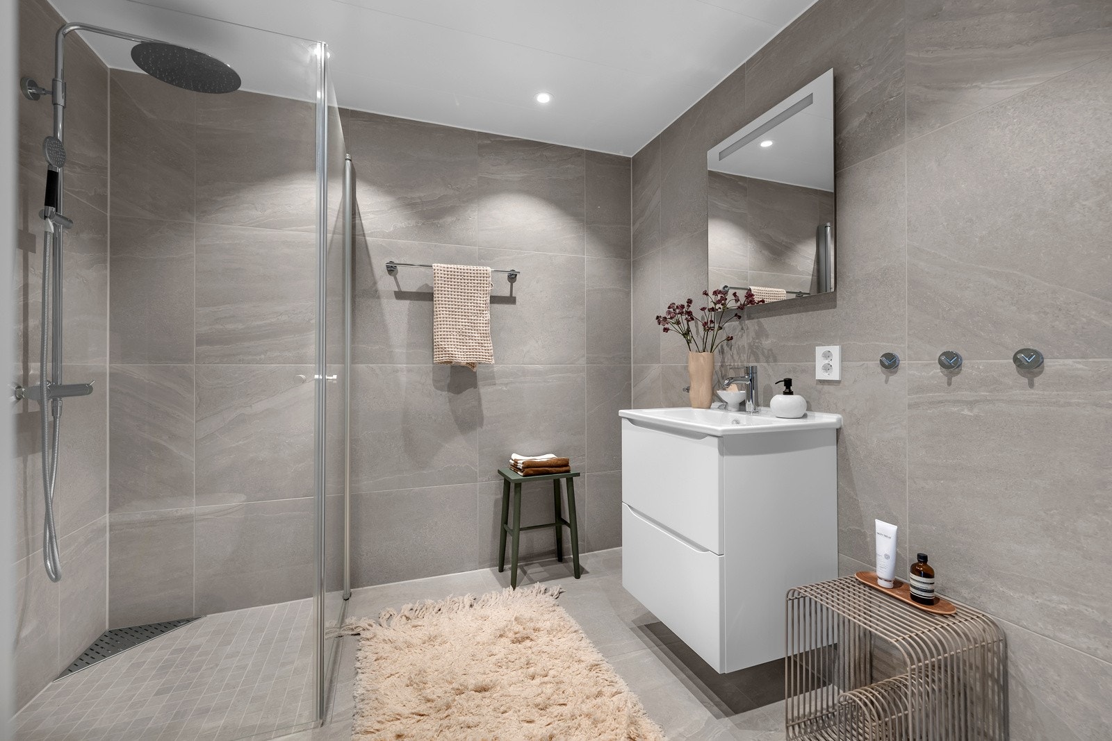 Badet er flislagt på gulv og vegger. Innfellbare dusjdører, innredning med heldekkende servant og lagring i kolonialskuffer m.m. Galleribilde