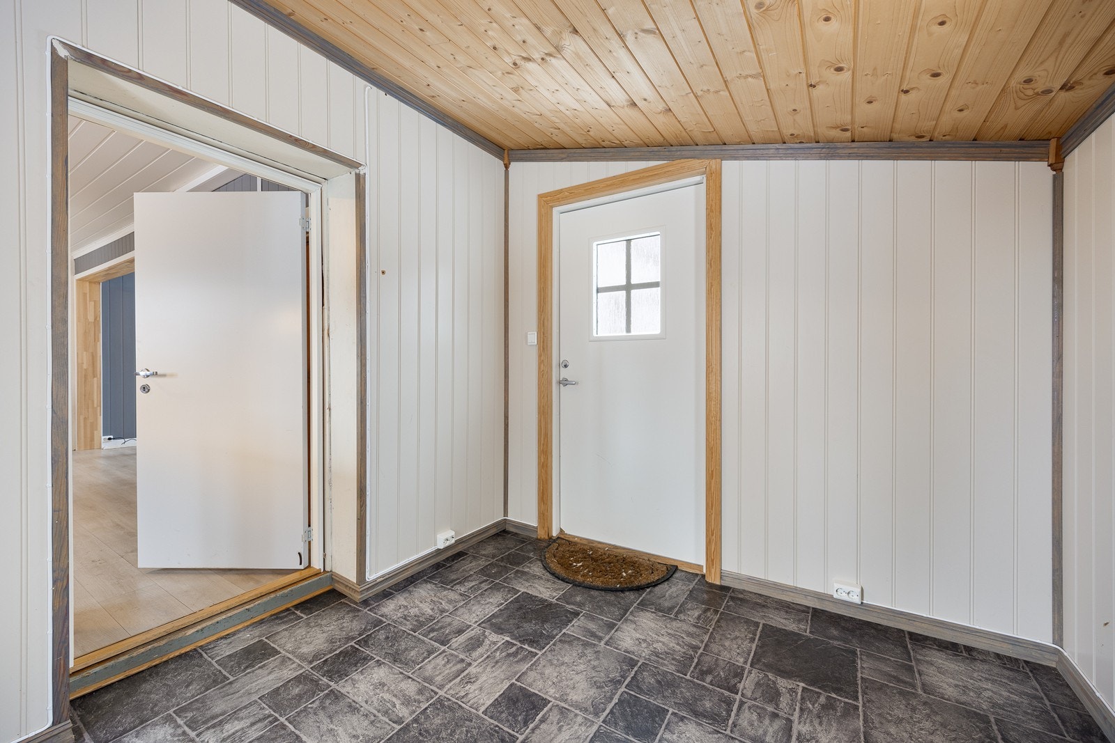 Entréen har hvitmalte panelvegger og grå laminatfliser på gulvet. Det er god plass til garderobeløsninger. Galleribilde