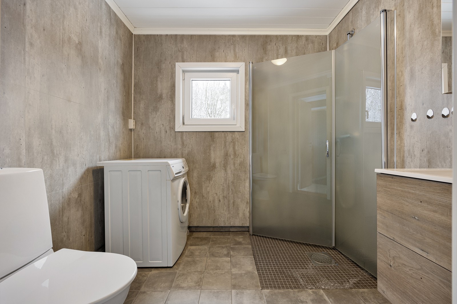 Badet er innredet med grå fliser på gulvet med lun gulvvarme, og på veggene er det grå våtromsplater. Galleribilde