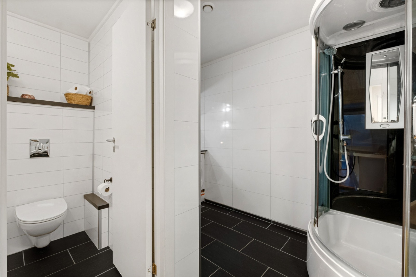 Badet ble modernisert i 2016 og har et tidsriktig uttrykk. Rommet har koksgrå gulvfliser, gulvvarme og hvite baderomsplater på veggene med flismønster. Galleribilde