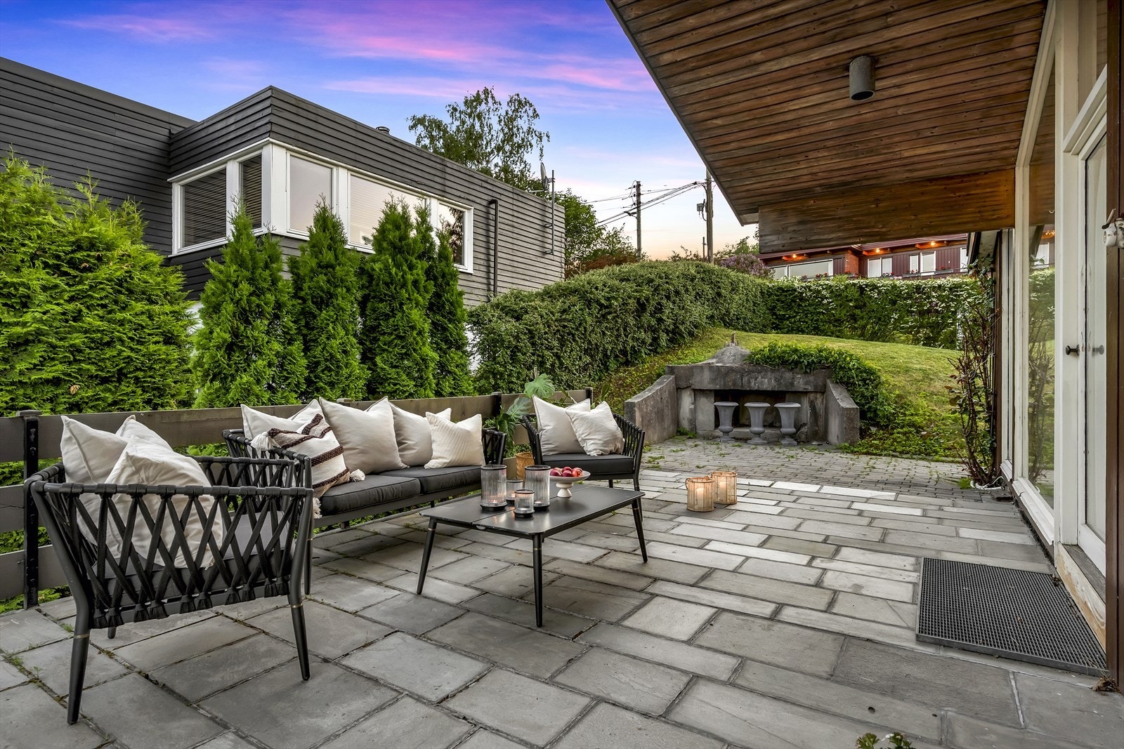 Fra takterrassen er det en skiferhellebelagt uteplass på siden av huset. Her delvis overbygget og med inngang til spisestuen. Galleribilde