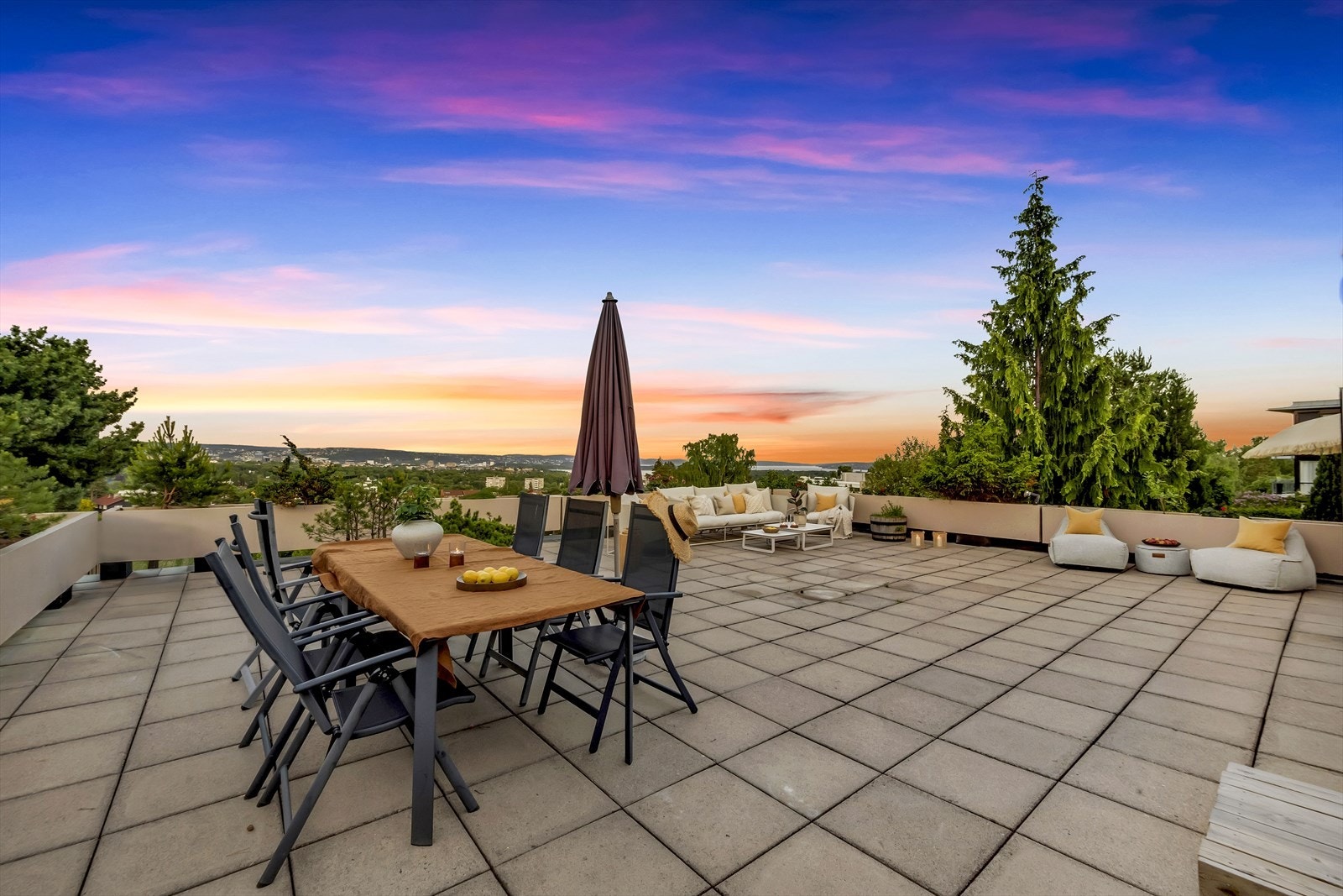 Kveldsstemning på terrassen. Gulvet er belagt med betongheller og det er støpte plantekasser som gjerde rundt terrassen. Galleribilde