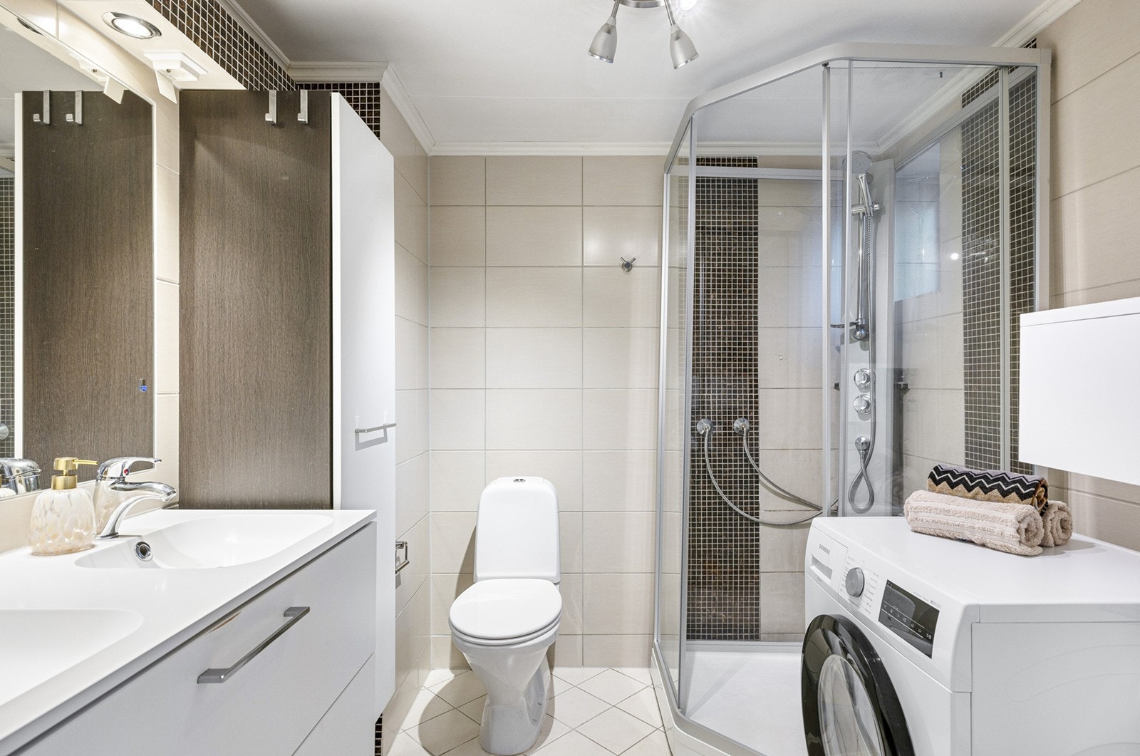 Pent baderom med fliser på gulv og vegger, og opplegg for vaskemaskin. Innredningen består av et underskap/sideskap, dobbel servant, speil, lys og stikk og et dusjkabinett. Ny ventilasjon i februar 2023. Galleribilde