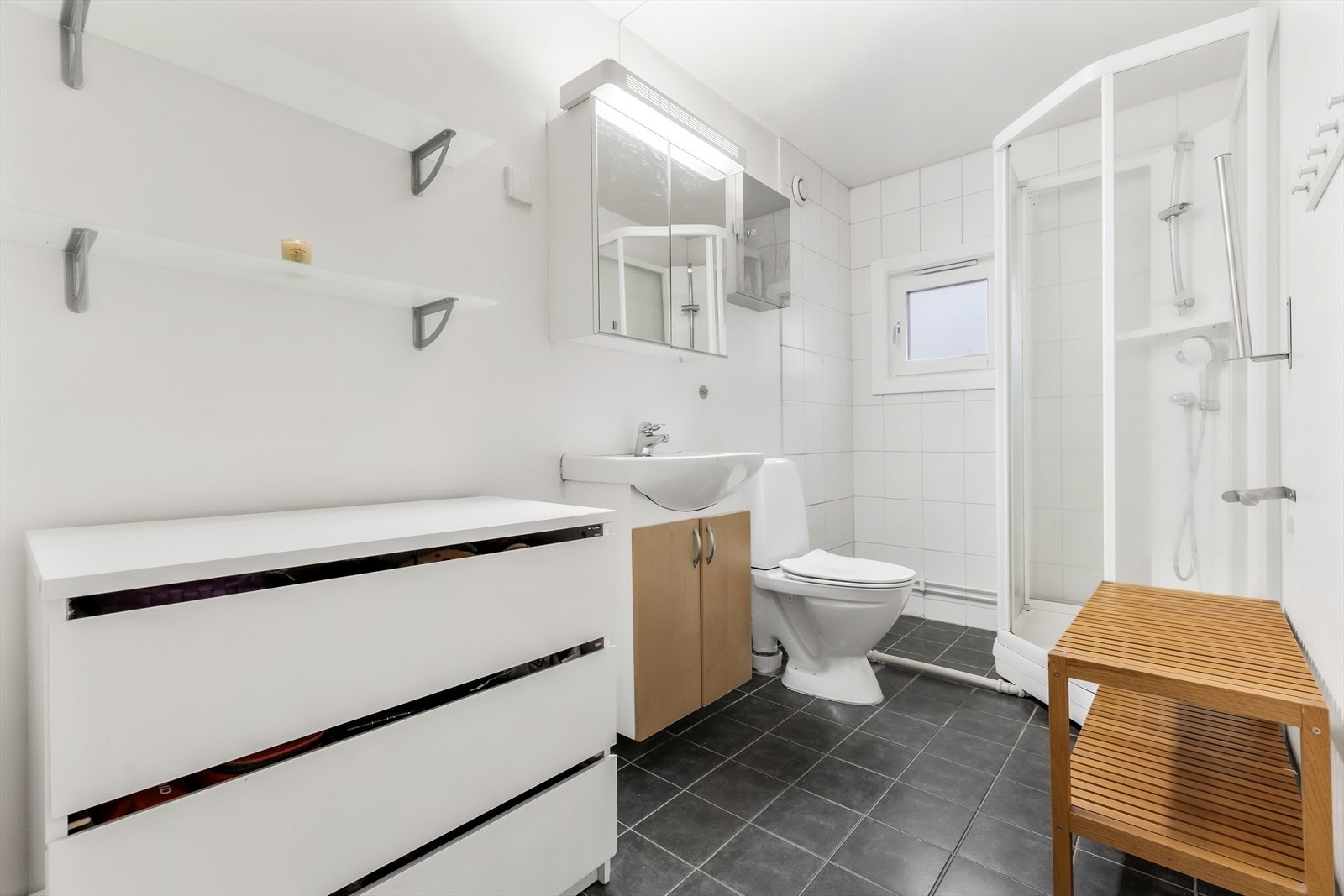 Flislagt bad med varmekabler i gulv. Badet består av servant med underskaper, speilskap, WC og dusjkabinett. Galleribilde