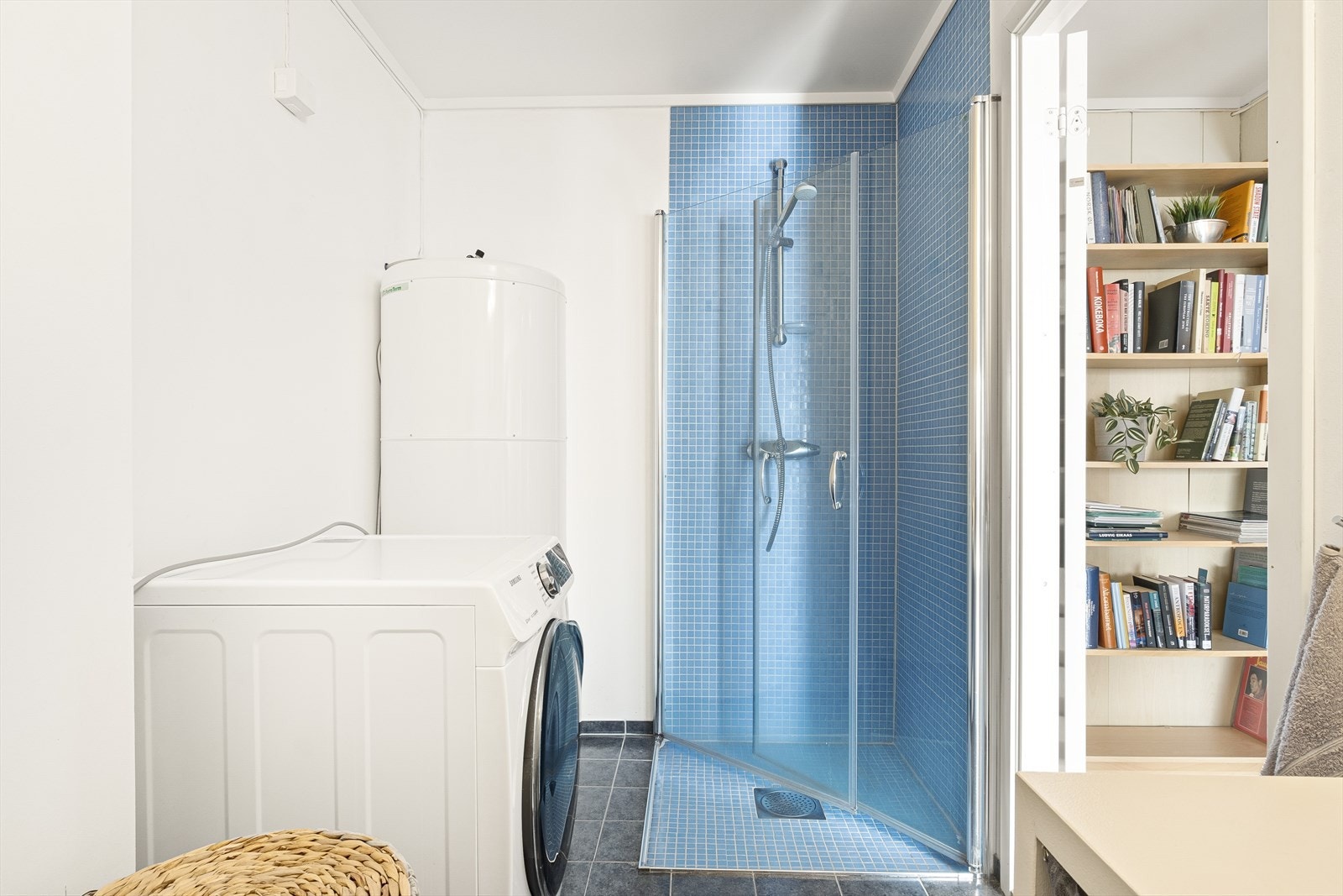 Badet er innredet med veggmontert wc, servant og dusjhjørne med svingbare dører. Her finner man også varmtvannsberederen og opplegg til vaskemaskin. Galleribilde