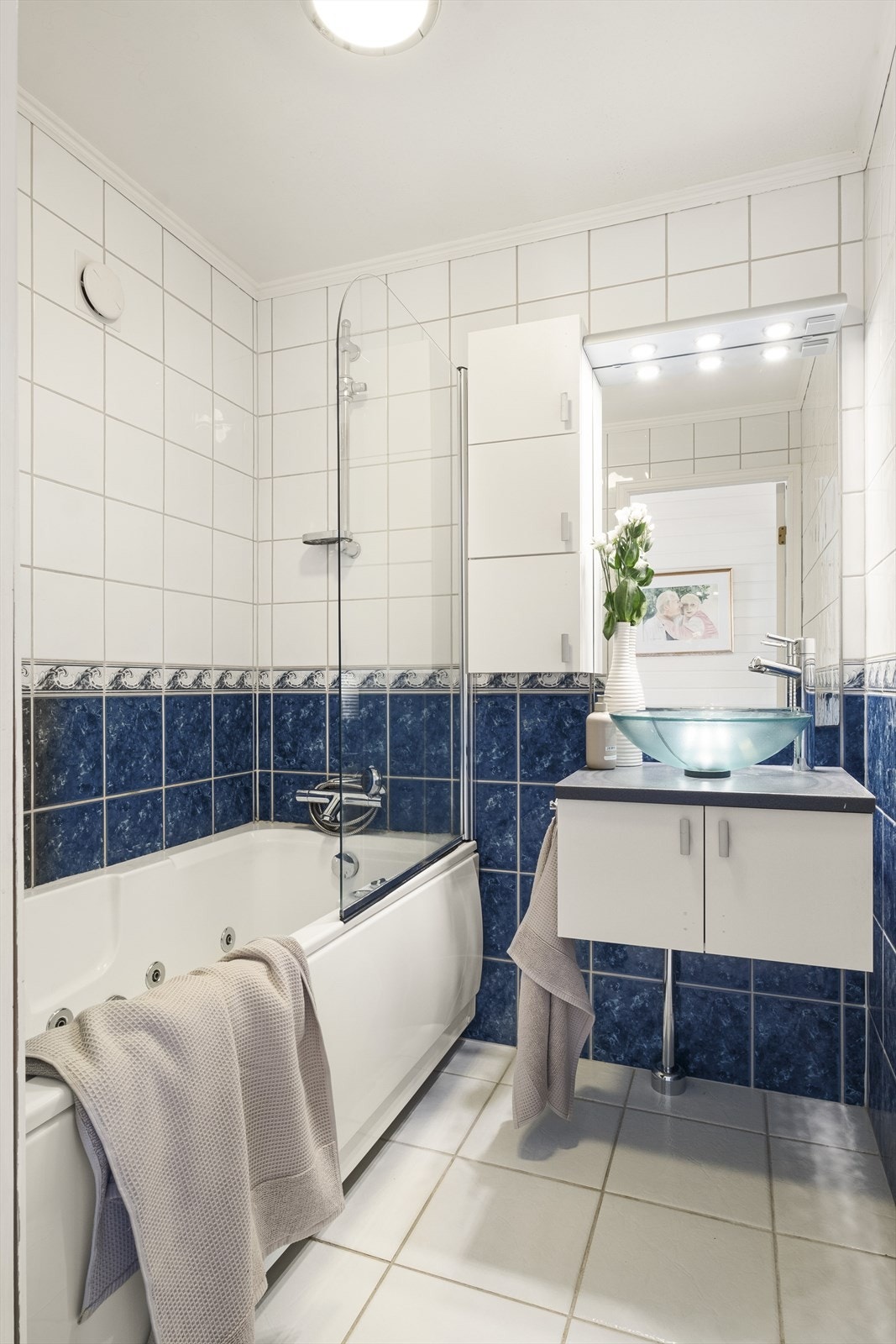 Pent bad med flislagte overflater og varmekabler i gulv. Badet innehar følgende: servant på skapinnredning og badekar med håndholdt spylefunksjon. Det er naturlig avtrekk og tilstrekkelig luftespalte for tilluft under dørbladet til baderomsdøren. Galleribilde