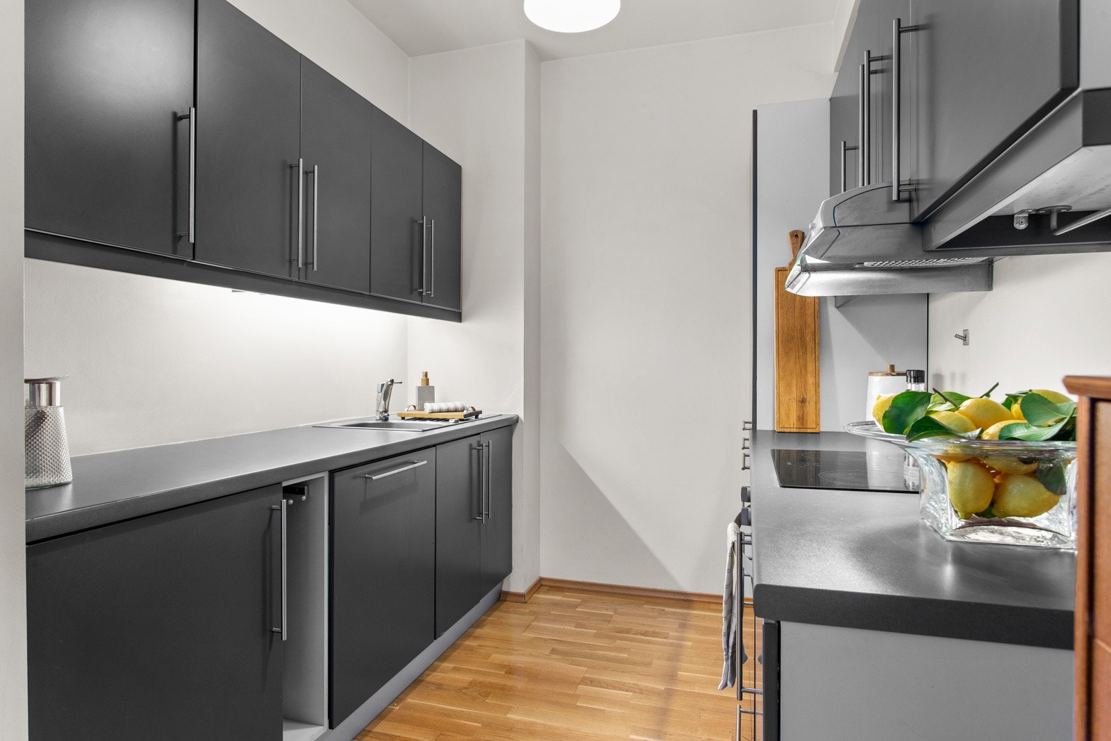 Innredningen har glatte fronter i en dyp gråfarge, benkeplate i laminat med nedfelt kum i rustfritt stål og kromfarget blandebatteri. Galleribilde