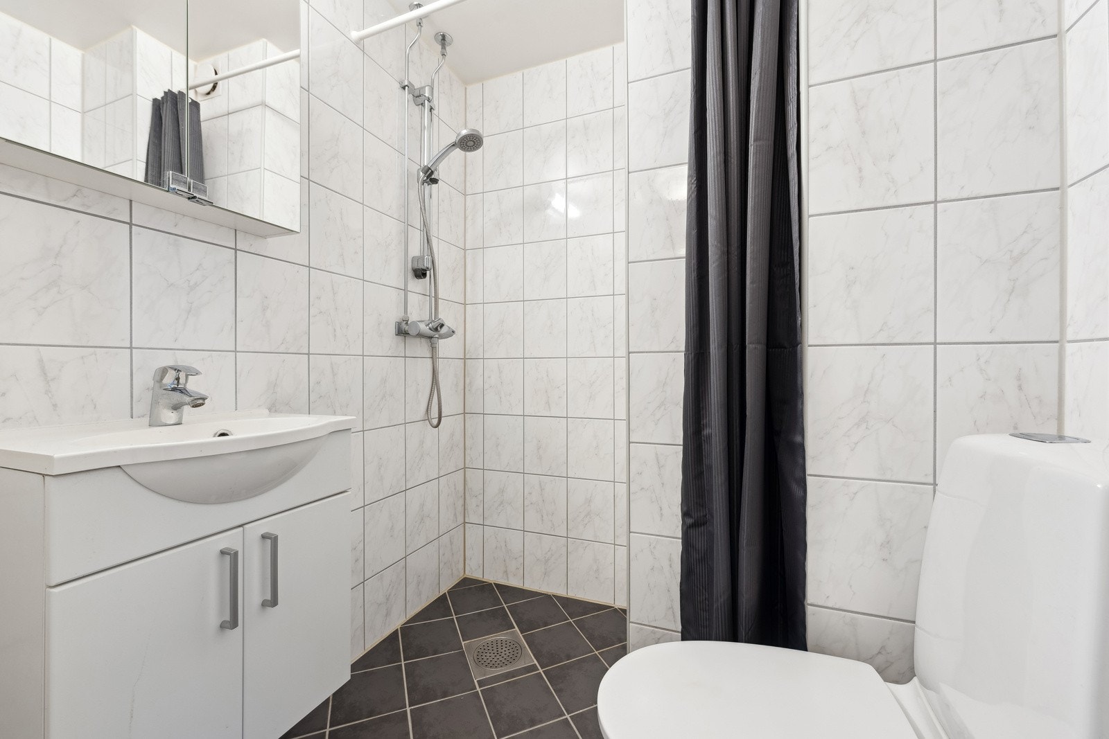 Pent og velholdt bad med servant med underskap, dusj og toalett. Galleribilde