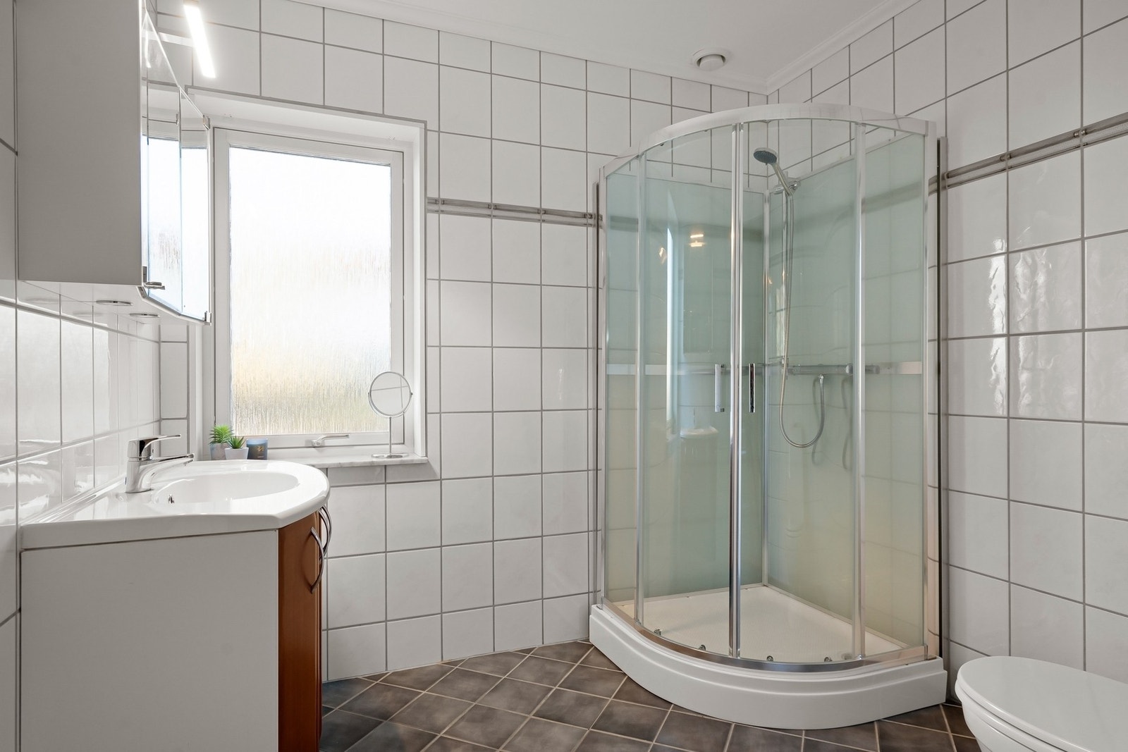 Badet i 1. etasje er flislagt og innredet med nedfelt servant, dusjkabinett og toalett. Det er vannbåren varme i gulvet. Galleribilde