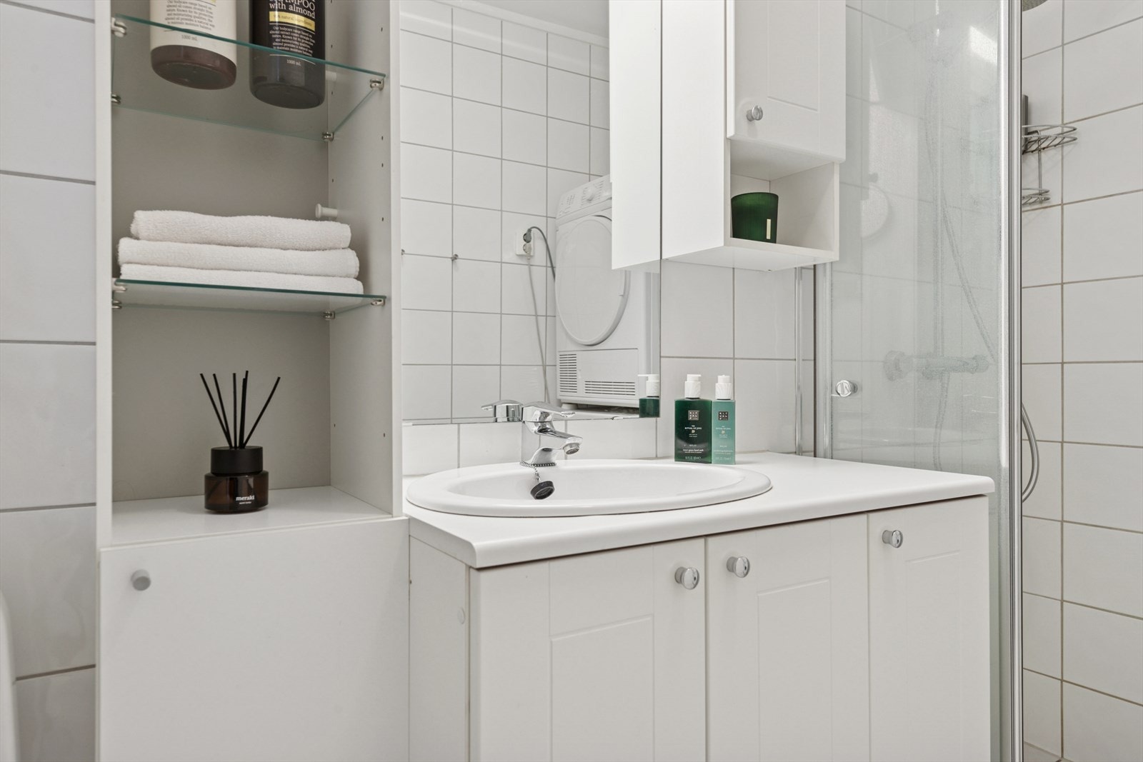 Badet har servant med underskap, speil med tilhørende belysning, dusjhjørne, gulvmontert wc og opplegg for vaskemaskin. Galleribilde