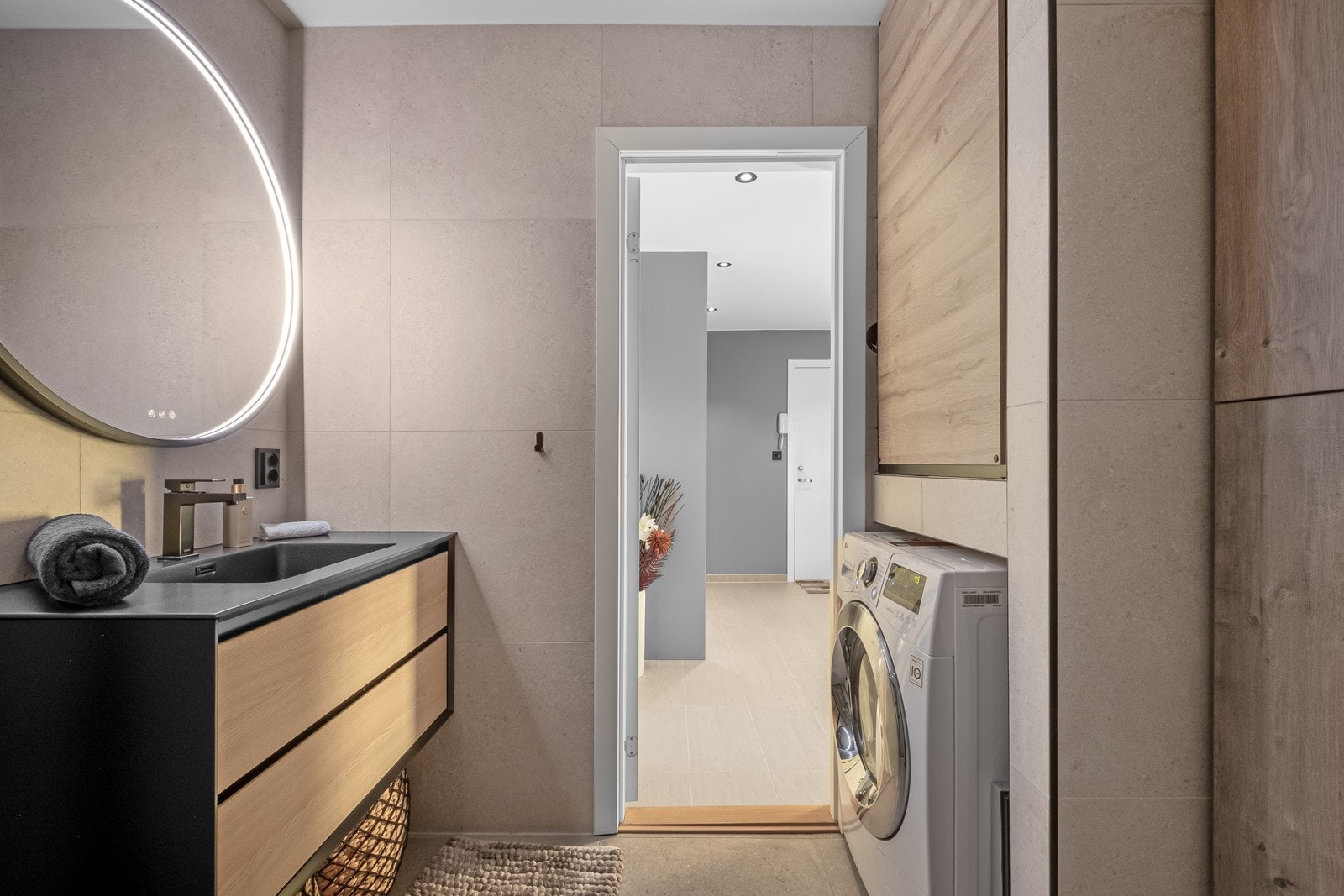 Badet har store fliser på vegger og gulv, og underliggende varmekabler. Det er opplegg for vaskemaskin. Galleribilde