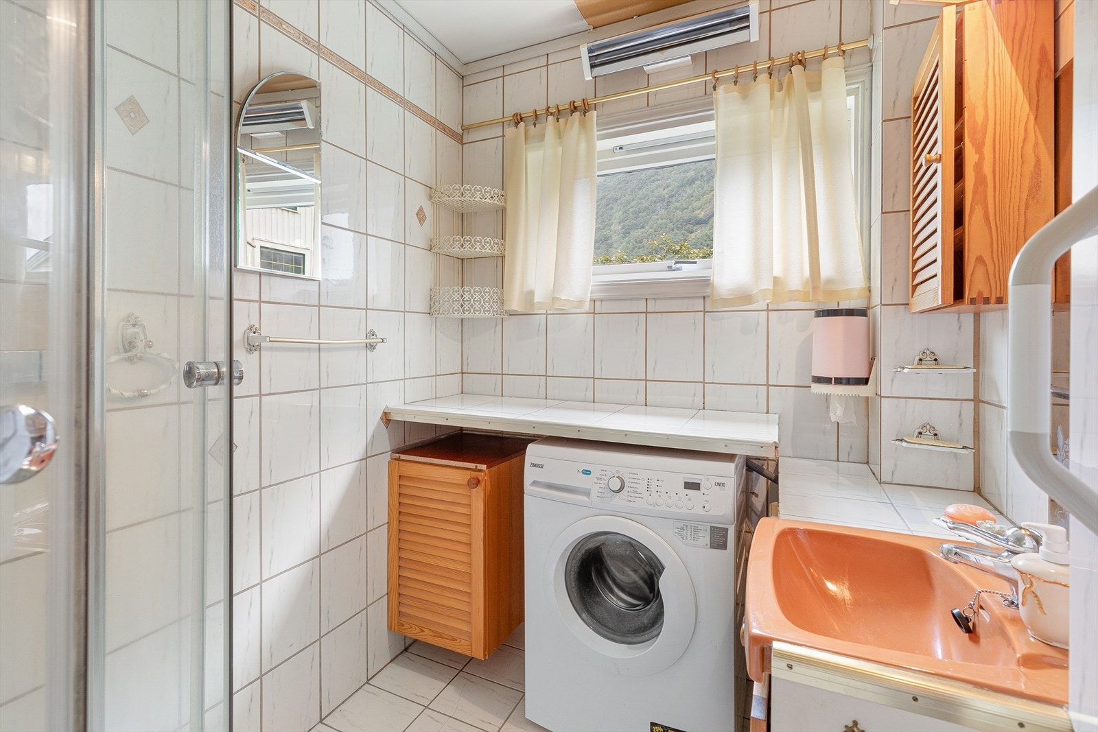 Badet er heilflisa og utstyrt med dusjhjørne, servant med innredning og opplegg for vaskemaskin. Galleribilde