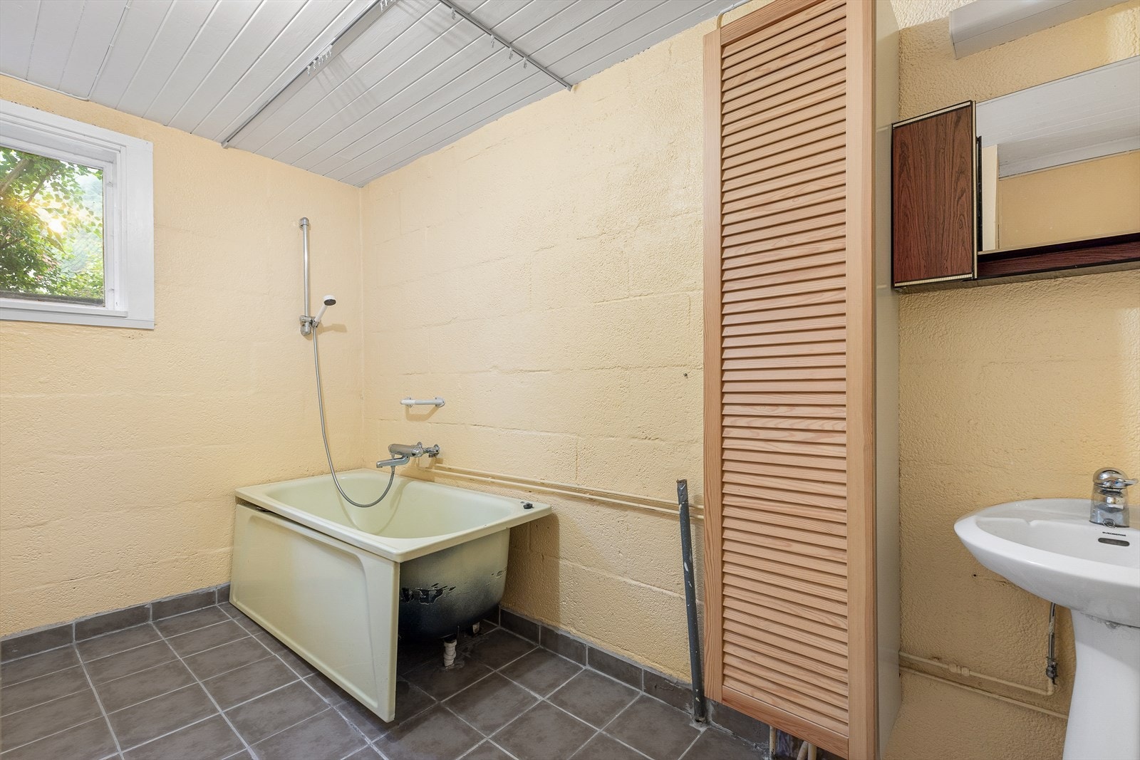 Enkelt vaskerom/bad utstyrt med badekar, servant og opplegg for vaskemaskin. Galleribilde